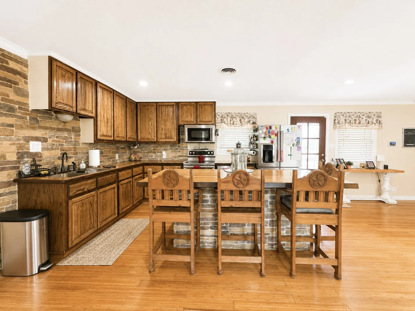 Spacious kitchen featuring wood-finish flooring, stone veneer backsplash, and natural wood cabinetry