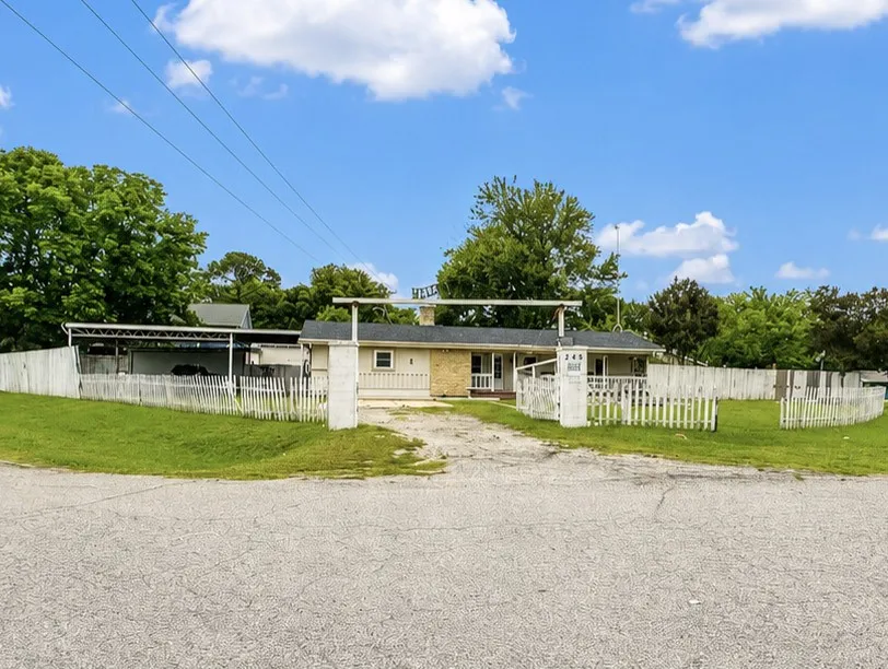 Single-story residence featuring a covered front porch, white picket fencing, and a gravel driveway