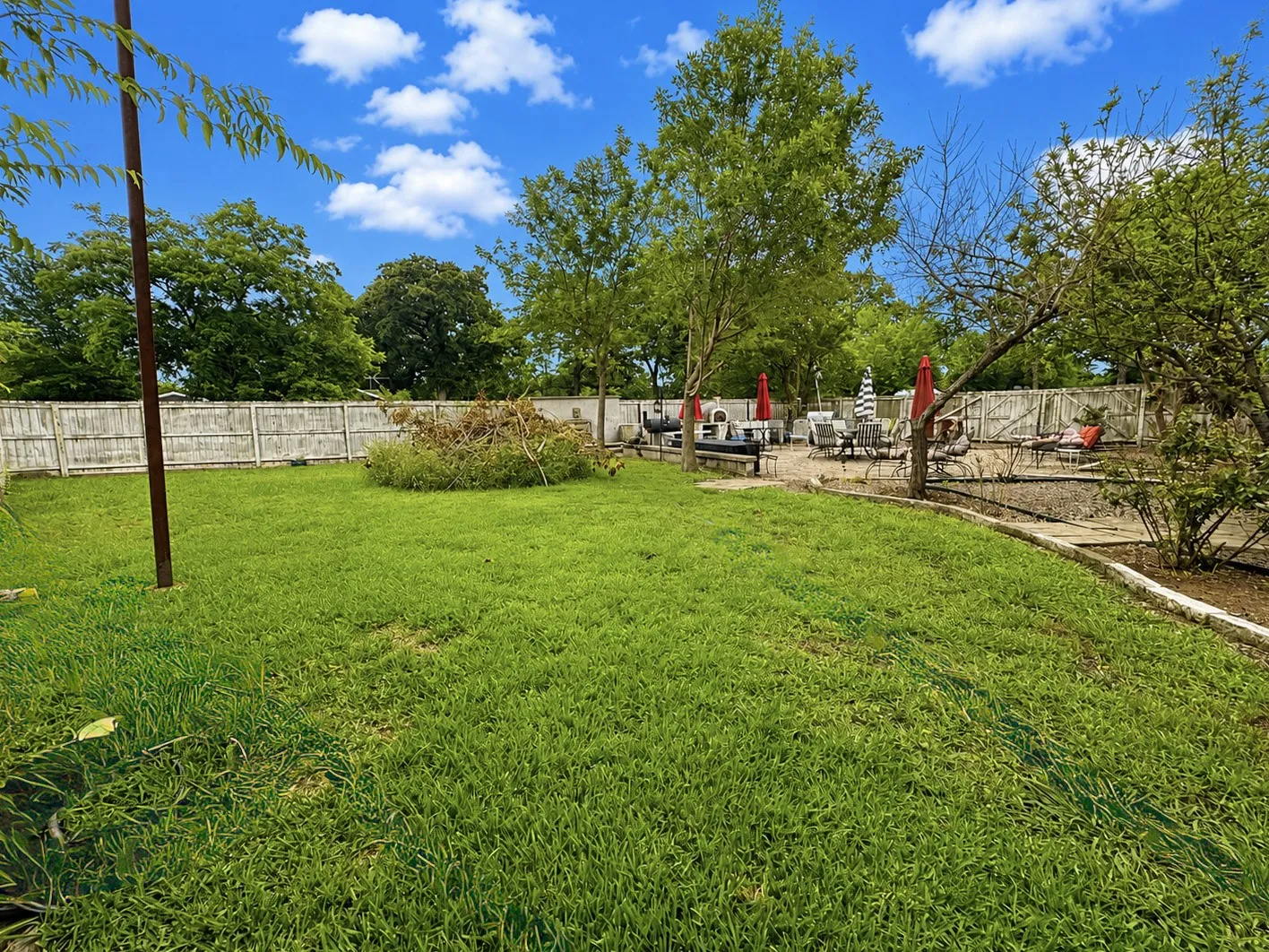 Expansive backyard featuring a large grassy area, wooden privacy fencing, and a dedicated patio space