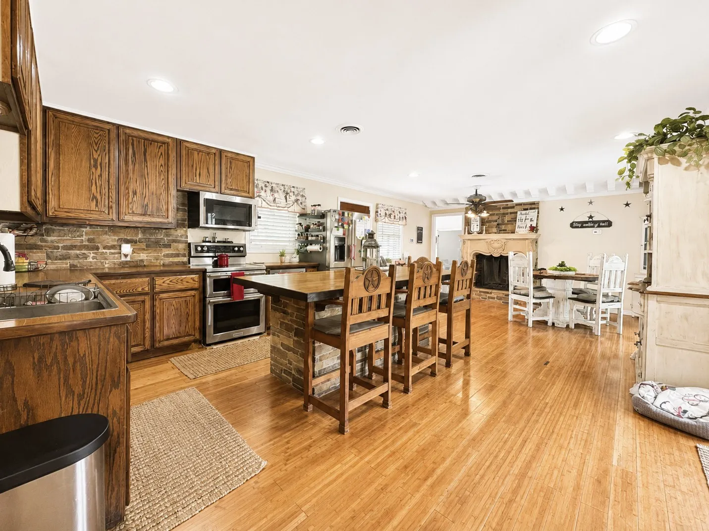 Open-concept kitchen and dining area featuring wood-finish flooring, recessed lighting, and a brick backsplash