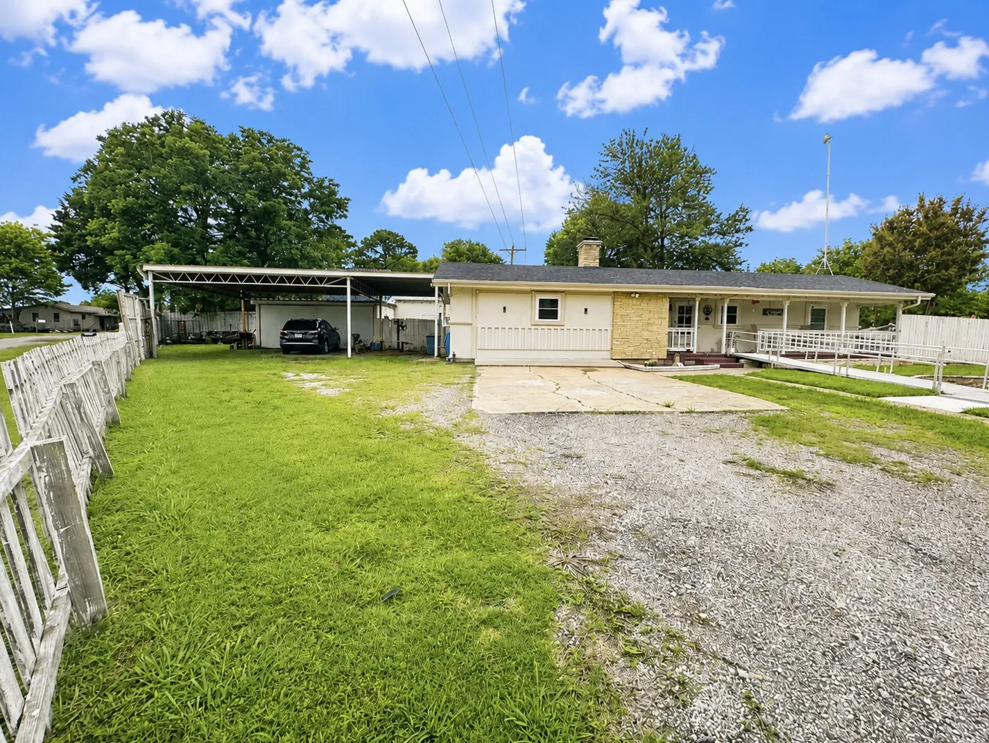 Carport and garage entrance on left. Large yard and gravel driveway.