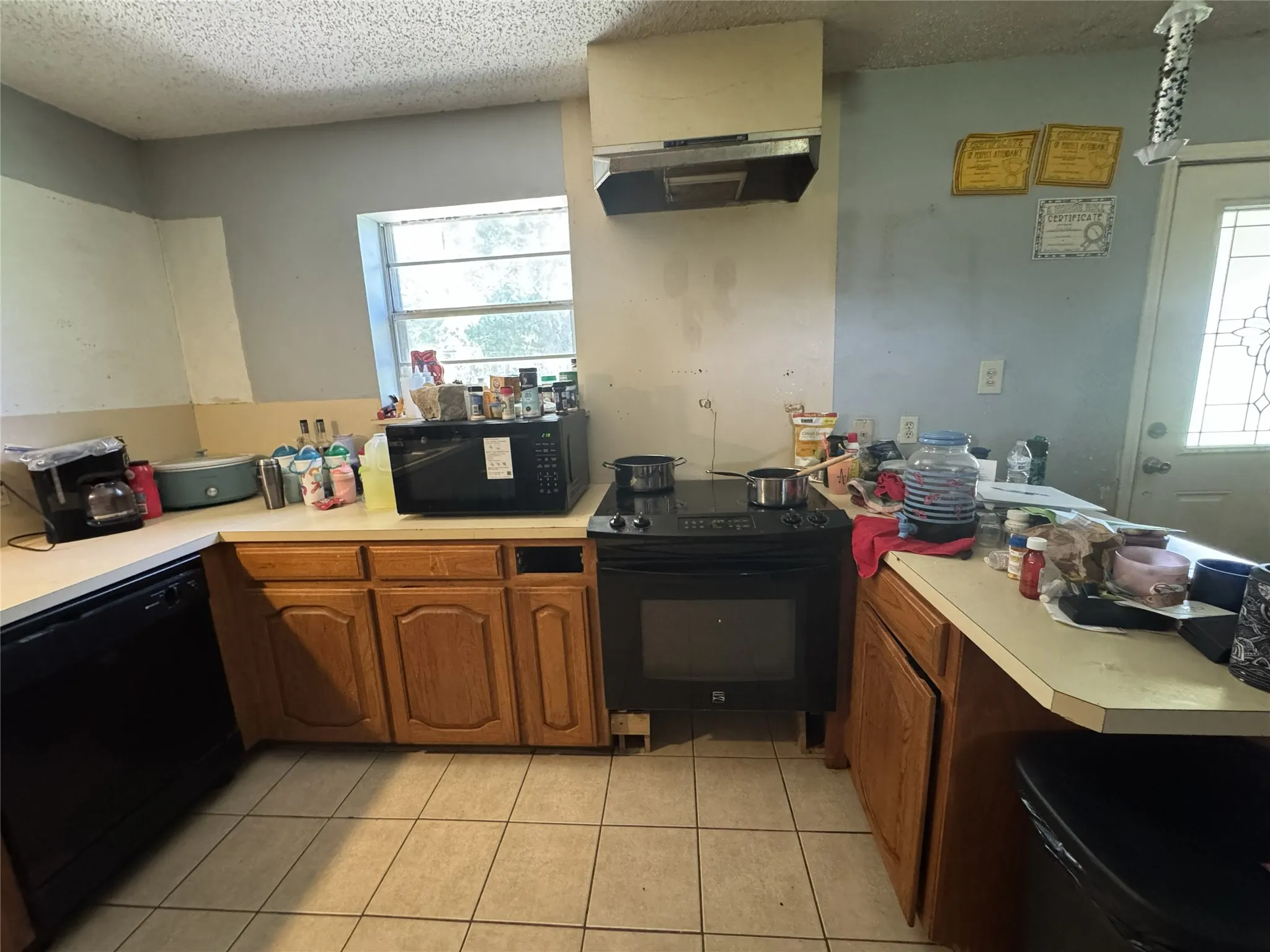 Kitchen featuring wood cabinetry, tiled flooring, an integrated black dishwasher, and a black electric range with an overhead exhaust hood