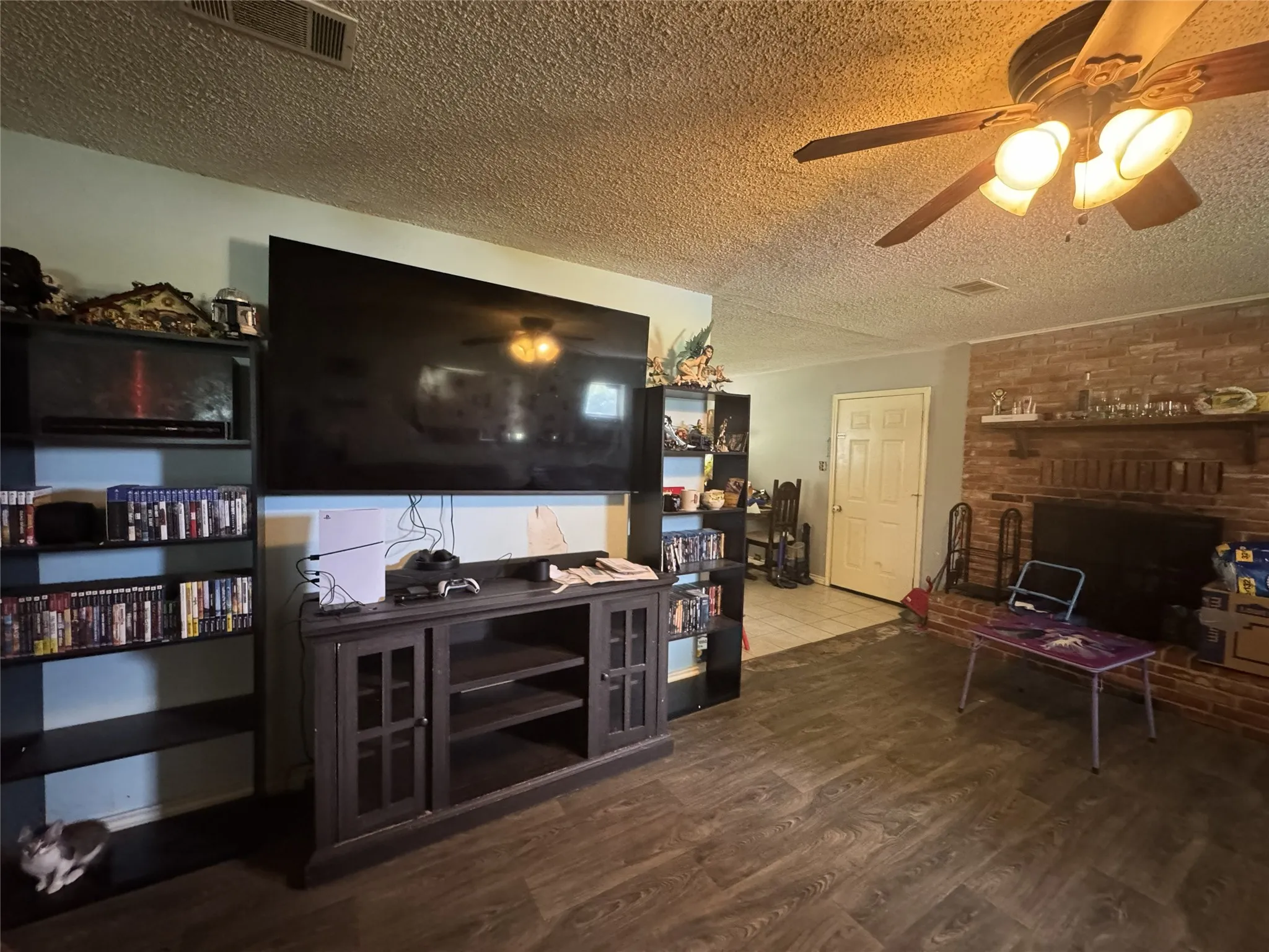 Living area featuring a brick fireplace, wood-finish flooring, and a ceiling fan with integrated lighting