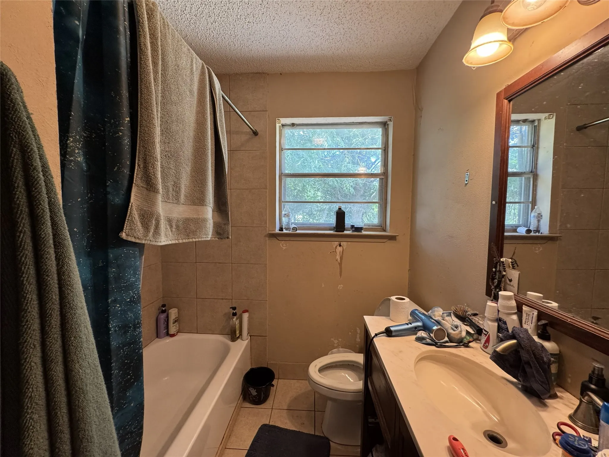 Bathroom with tile-surround bathtub, single pane window, vanity with integrated sink, and wall-mounted light fixture