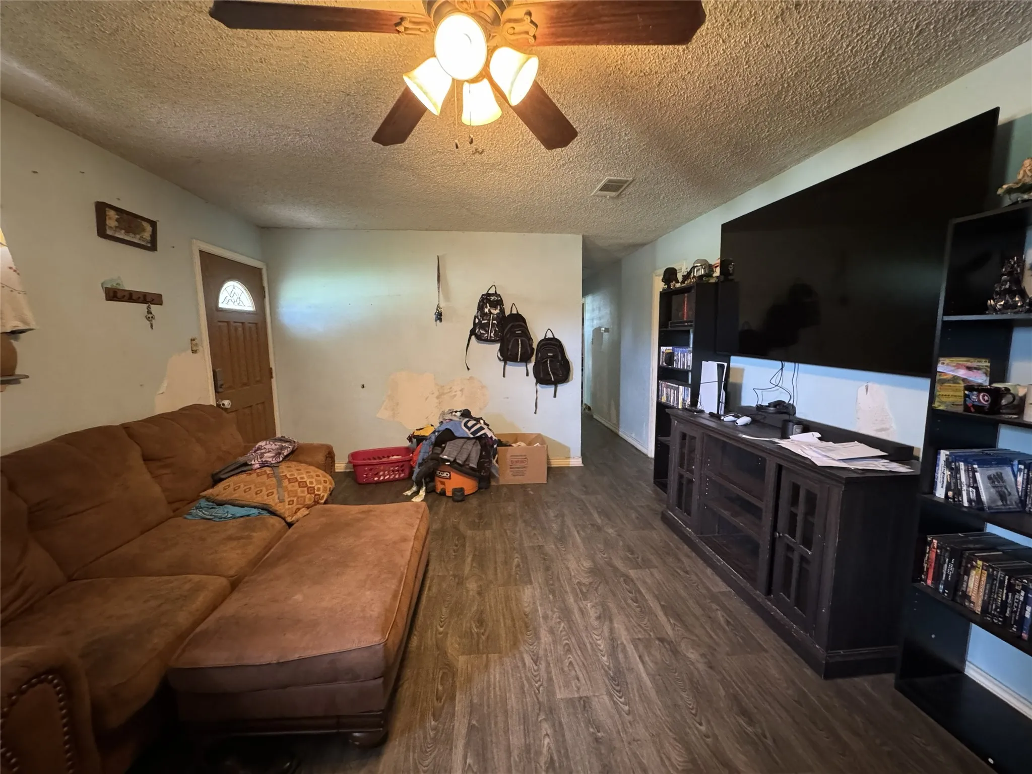 Living area featuring wood-finish flooring, a ceiling fan with integrated lighting, and a paneled entry door with an arched glass insert