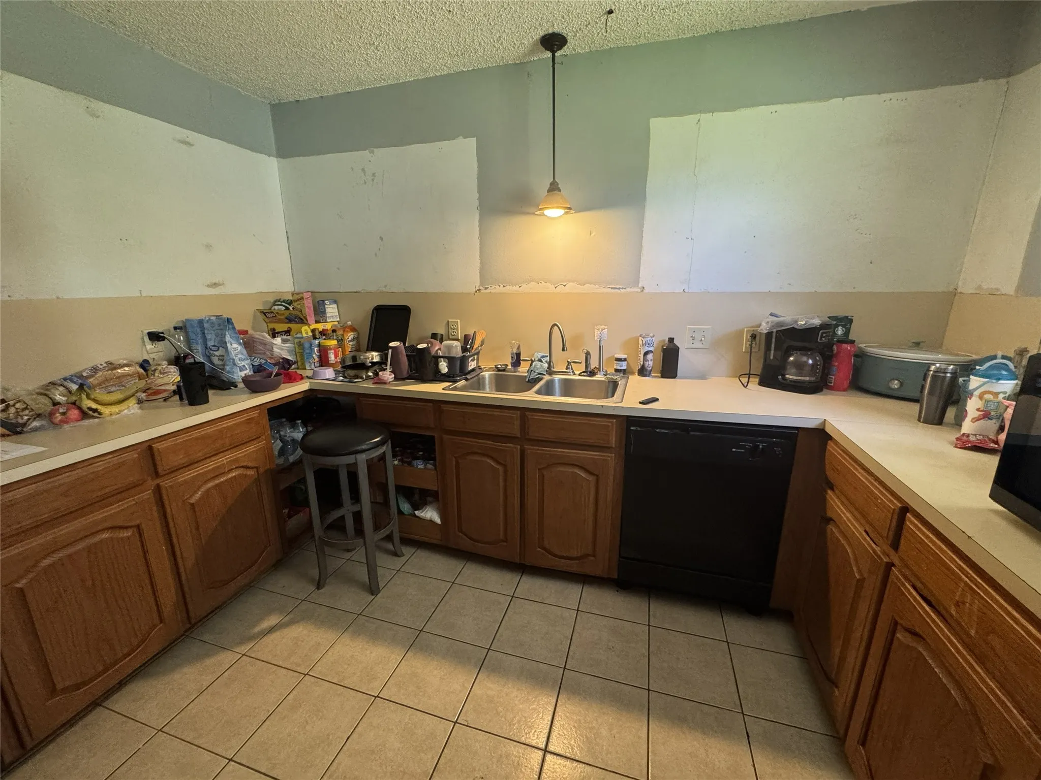 Kitchen featuring a double basin stainless steel sink, a black dishwasher, light-toned countertops, wood-finish cabinetry, and tiled flooring
