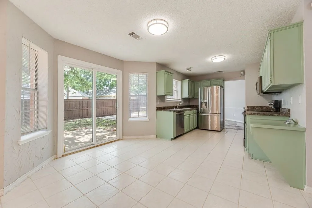 Kitchen and dining area featuring light green cabinetry, stainless steel appliances, dark countertops, and tile flooring
