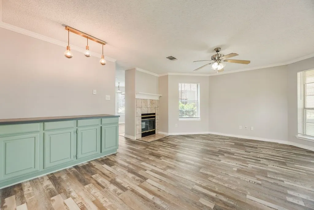 Open-concept living area featuring wood-finish flooring, a tiled fireplace with mantel, and multiple windows