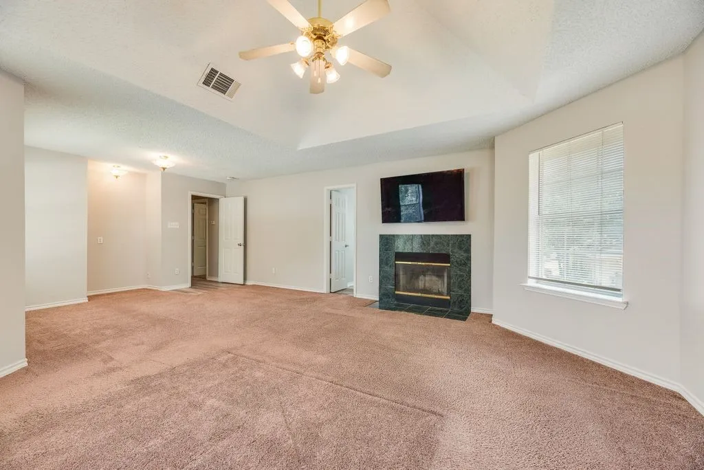 Spacious interior featuring a vaulted ceiling with a ceiling fan, a fireplace with a dark green surround, and light-colored carpeting