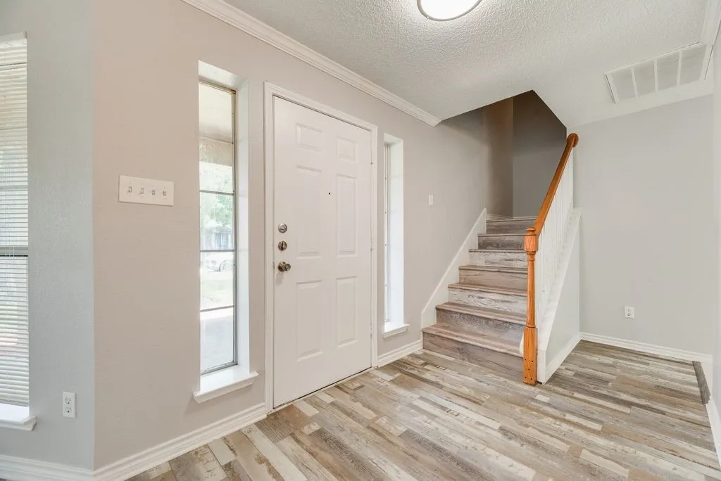Entryway featuring wood-finish flooring, a paneled entry door with sidelights, a staircase with a wood handrail, light gray wall paint, and white baseboards