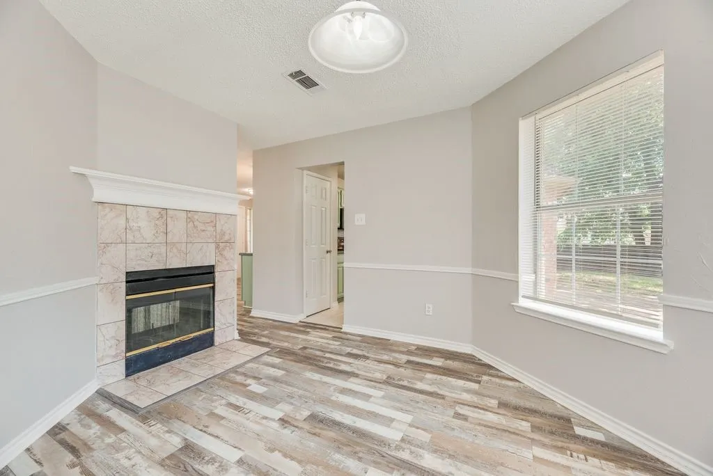 Living area featuring a tiled fireplace with a mantel, wood-finish flooring, and a window with blinds