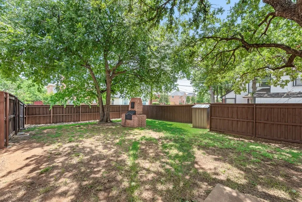 Expansive backyard featuring mature trees, a built-in brick grilling station, wood privacy fencing, and a storage shed