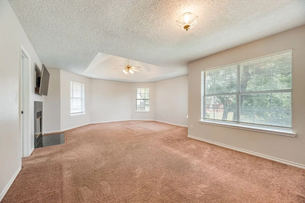 Spacious room featuring a tray ceiling, ceiling fan, and multiple windows with horizontal blinds