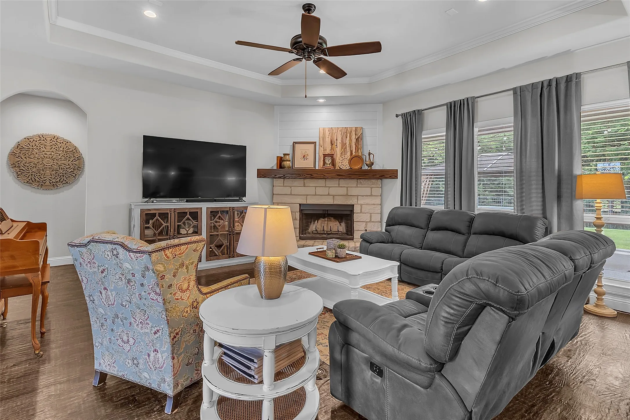 Spacious open-concept living area featuring crown molding, hand-scraped wood flooring, a tray ceiling with recessed lighting, ceiling fan and fireplace