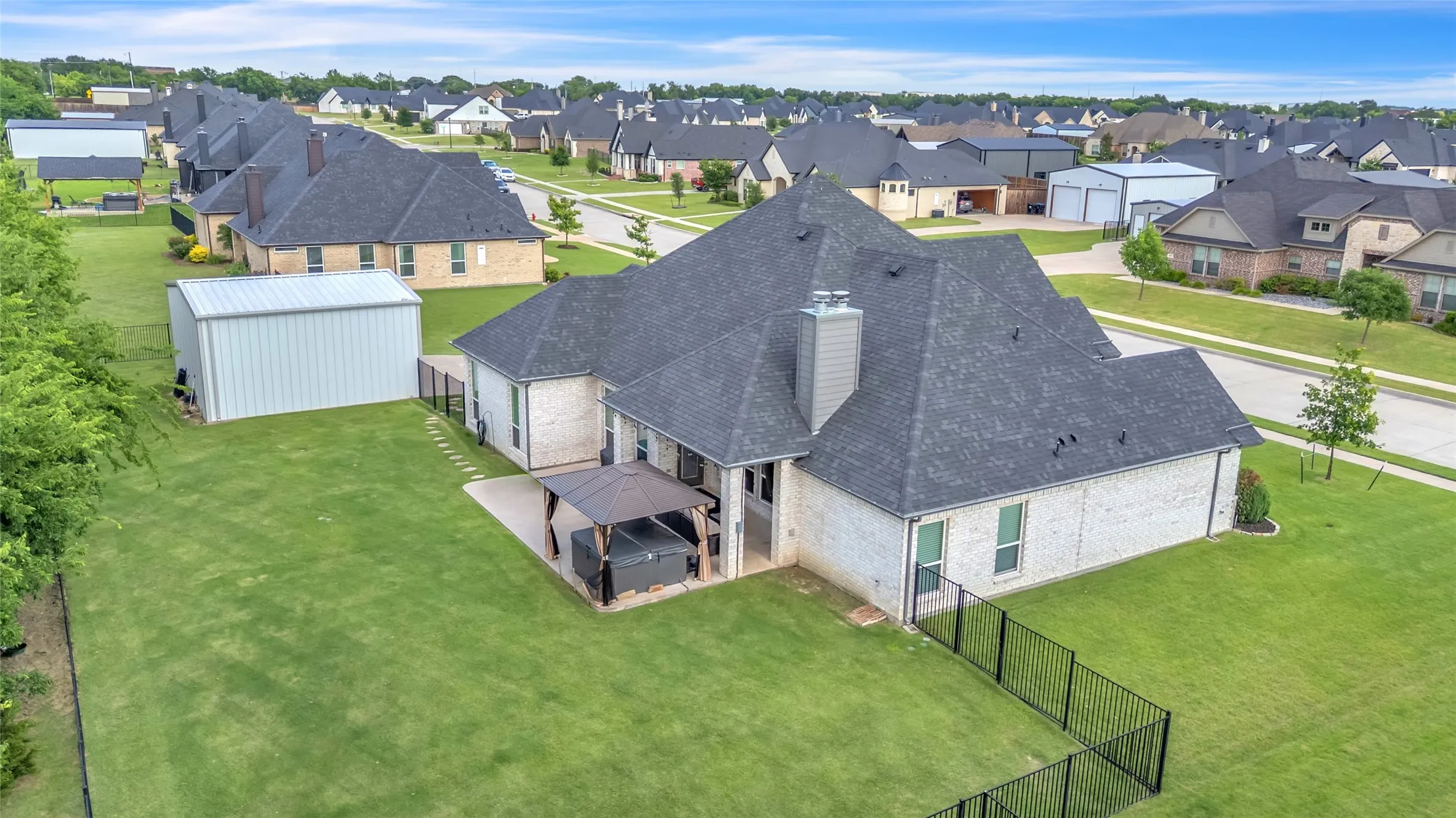 Expansive backyard featuring a manicured lawn, an extended concrete patio with a hot tub with gazebo, covered outdoor living area with fire place and a large detached metal storage building