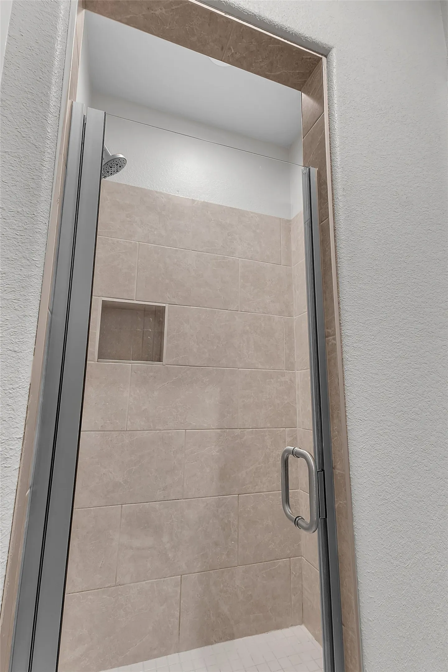 Shower enclosure featuring clear glass panels, a brushed metal handle, and neutral-toned rectangular wall tiles