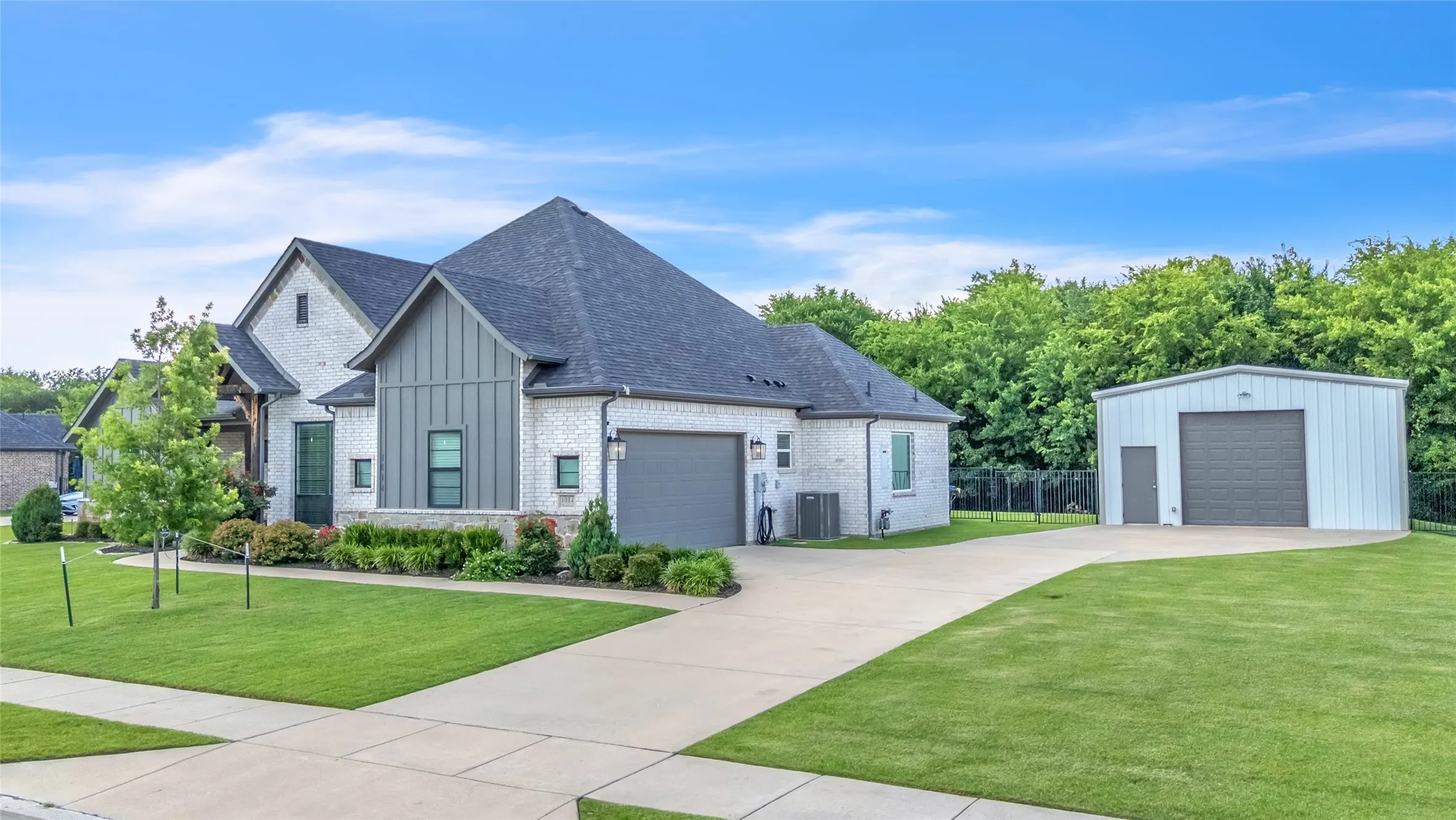 Contemporary brick and board-and-batten exterior featuring an attached two-car garage and a detached metal workshop with an additional garage door and loft for additional storage