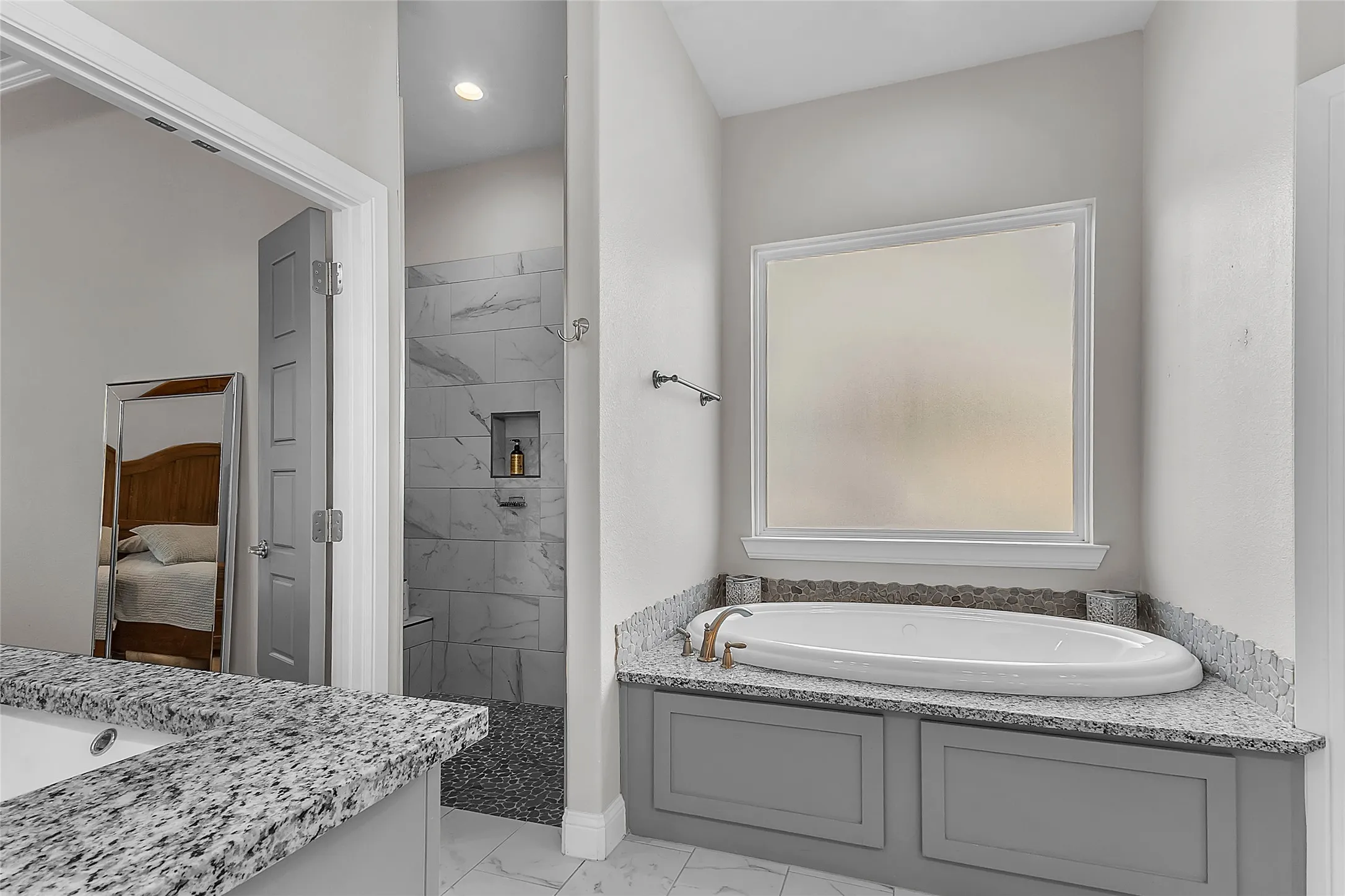 Spacious primary bathroom featuring a built-in jetted tub with granite surround, a separate glass-enclosed walk-in shower with tiled walls and pebble flooring, a frosted privacy window