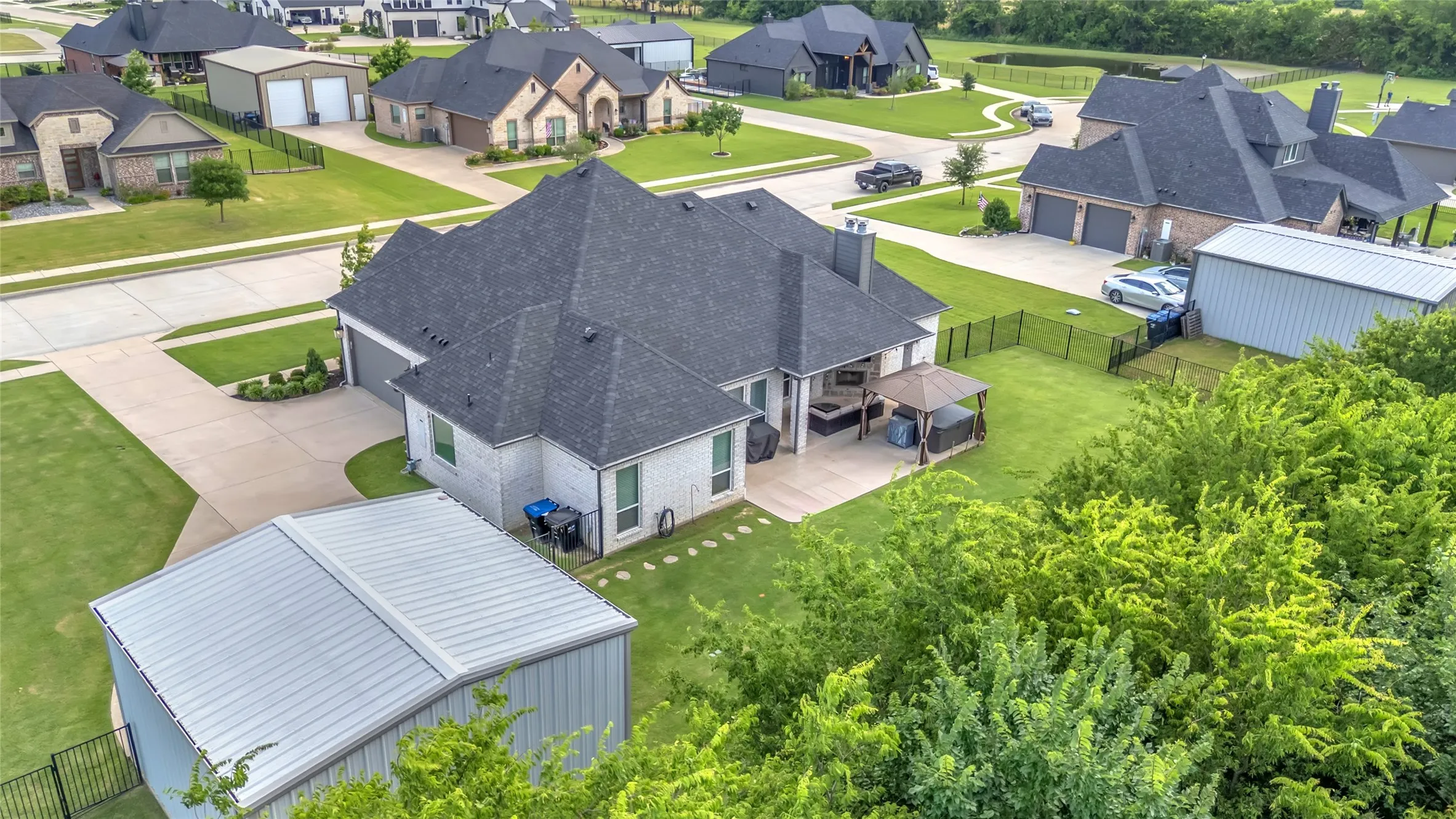Expansive backyard featuring a manicured lawn, an extended concrete patio with a hot tub with gazebo, covered outdoor living area with fire place and a large detached metal storage building