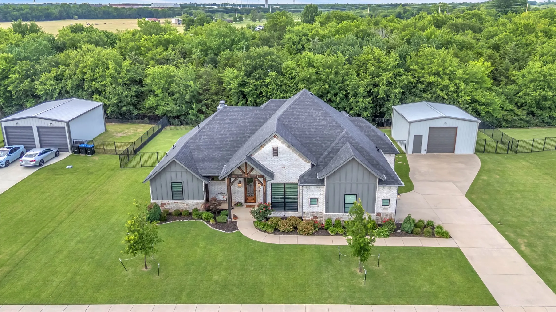 Aerial view of exterior of home on oversized,  tree-lined lot featuring large workshop and extended driveway