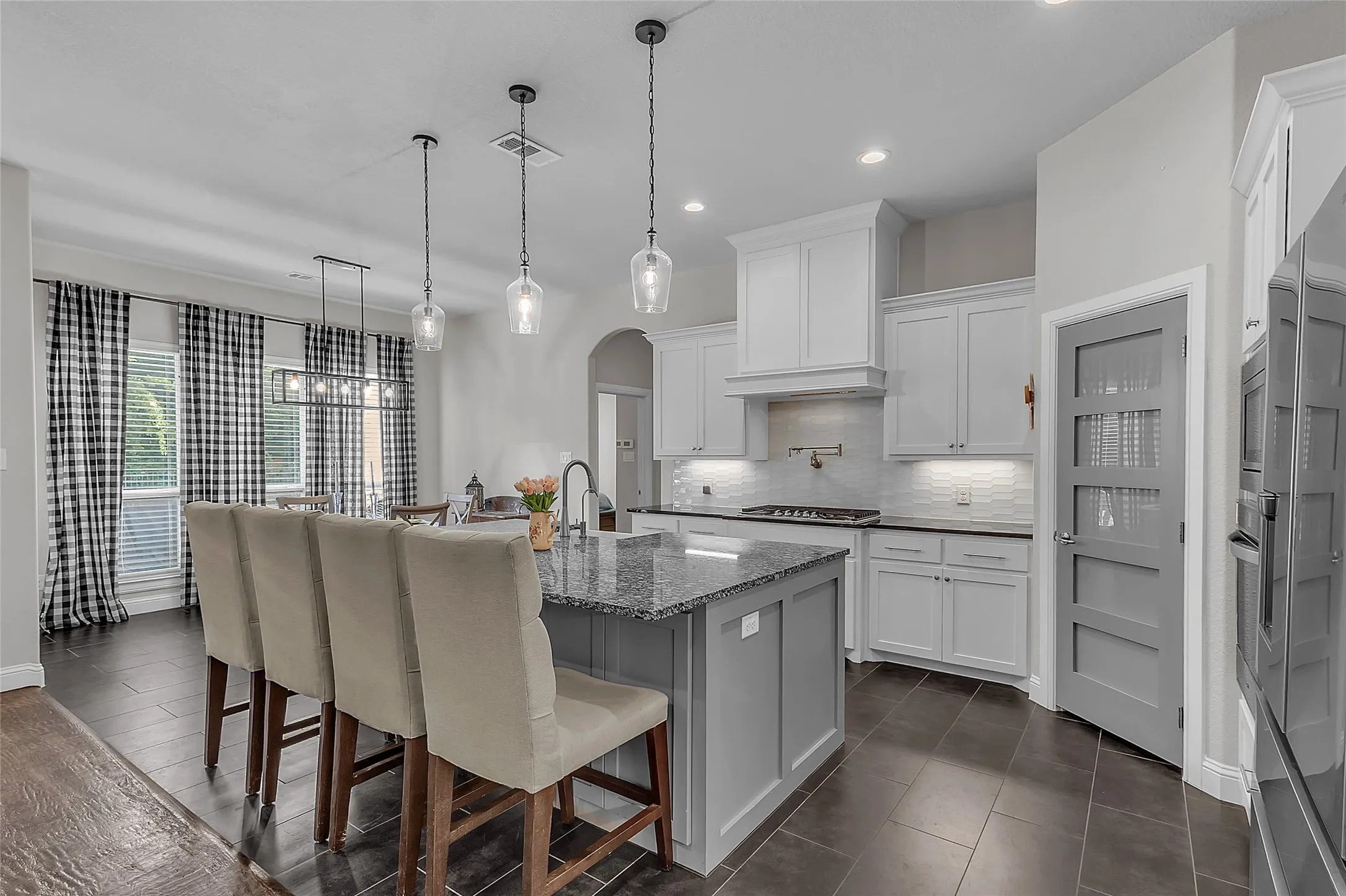 Kitchen featuring a large island with a granite countertop, shaker-style cabinetry with ample storage, integrated stainless steel appliances, and dark tile flooring