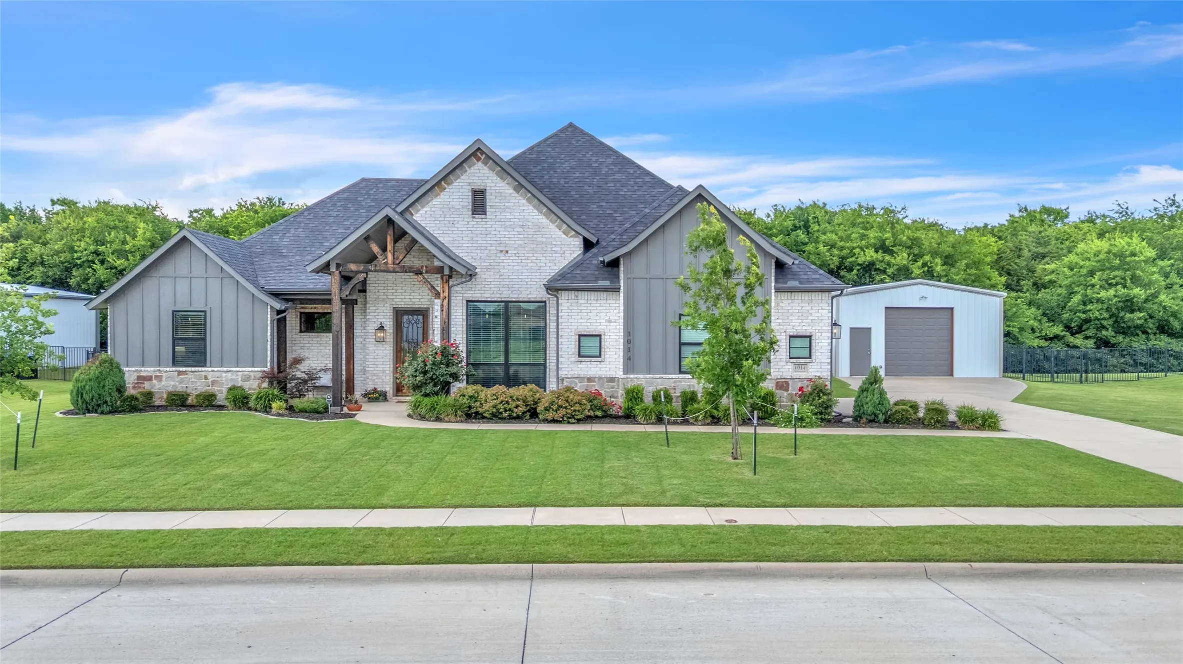Modern farmhouse style exterior featuring brick, board & batten siding, and a stone exterior. Also shown is the covered front porch and elevated landscaping.