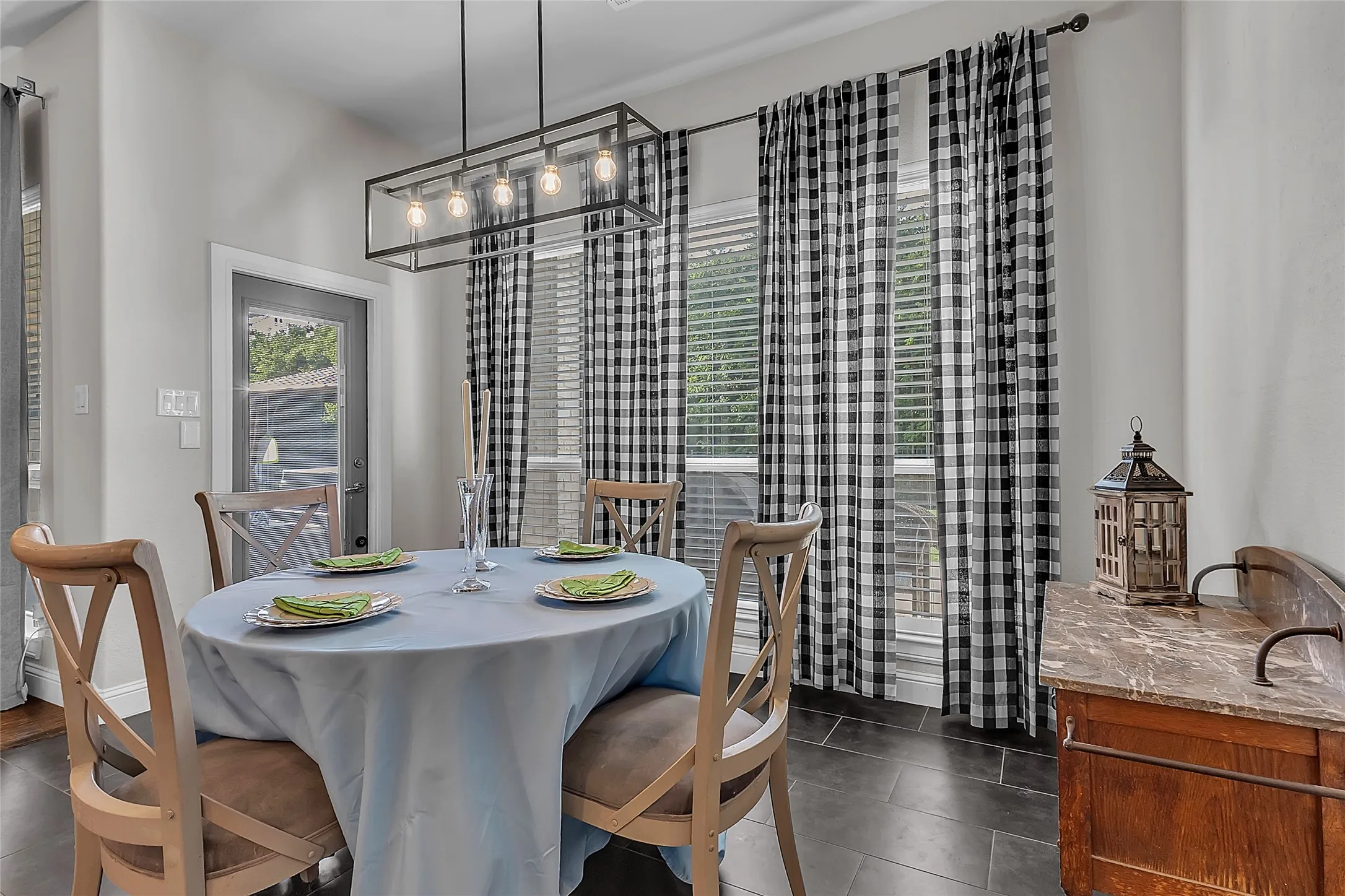 Dining area just off the kitchen featuring decorative lighting, dark tile flooring, windows looking out to backyard, and back door to covered porch area