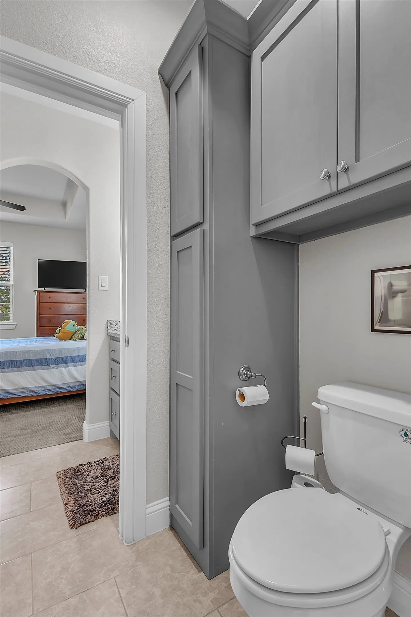 Bathroom featuring a built-in floor-to-ceiling cabinet, upper wall-mounted cabinetry, a toilet, and light-toned tile flooring