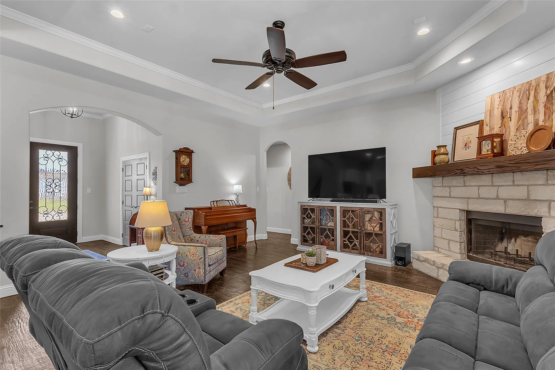 Spacious open-concept living area featuring, crown molding, hand-scraped wood flooring, a tray ceiling with recessed lighting, ceiling fan and fireplace