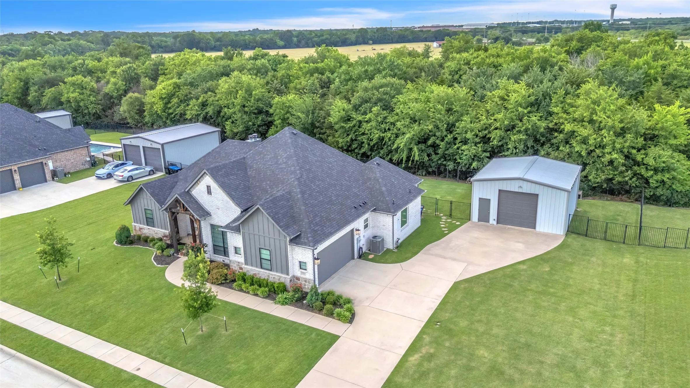 Modern farmhouse style exterior featuring brick, board & batten siding, and a stone exterior. Also shown is the extended driveway and 24x24 workshop and elevated landscaping.