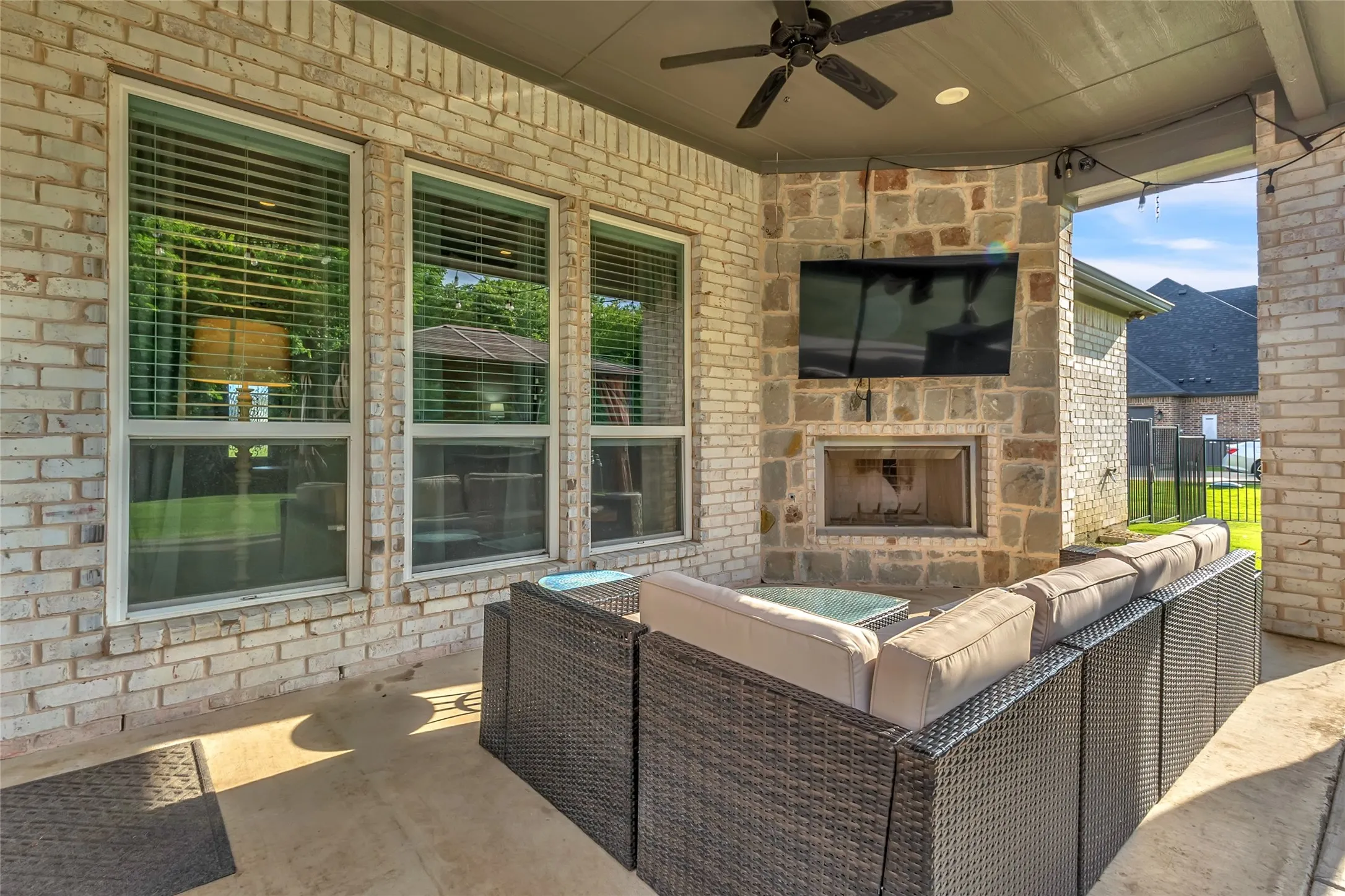Covered outdoor patio featuring a stone-clad fireplace, integrated television, and a ceiling fan