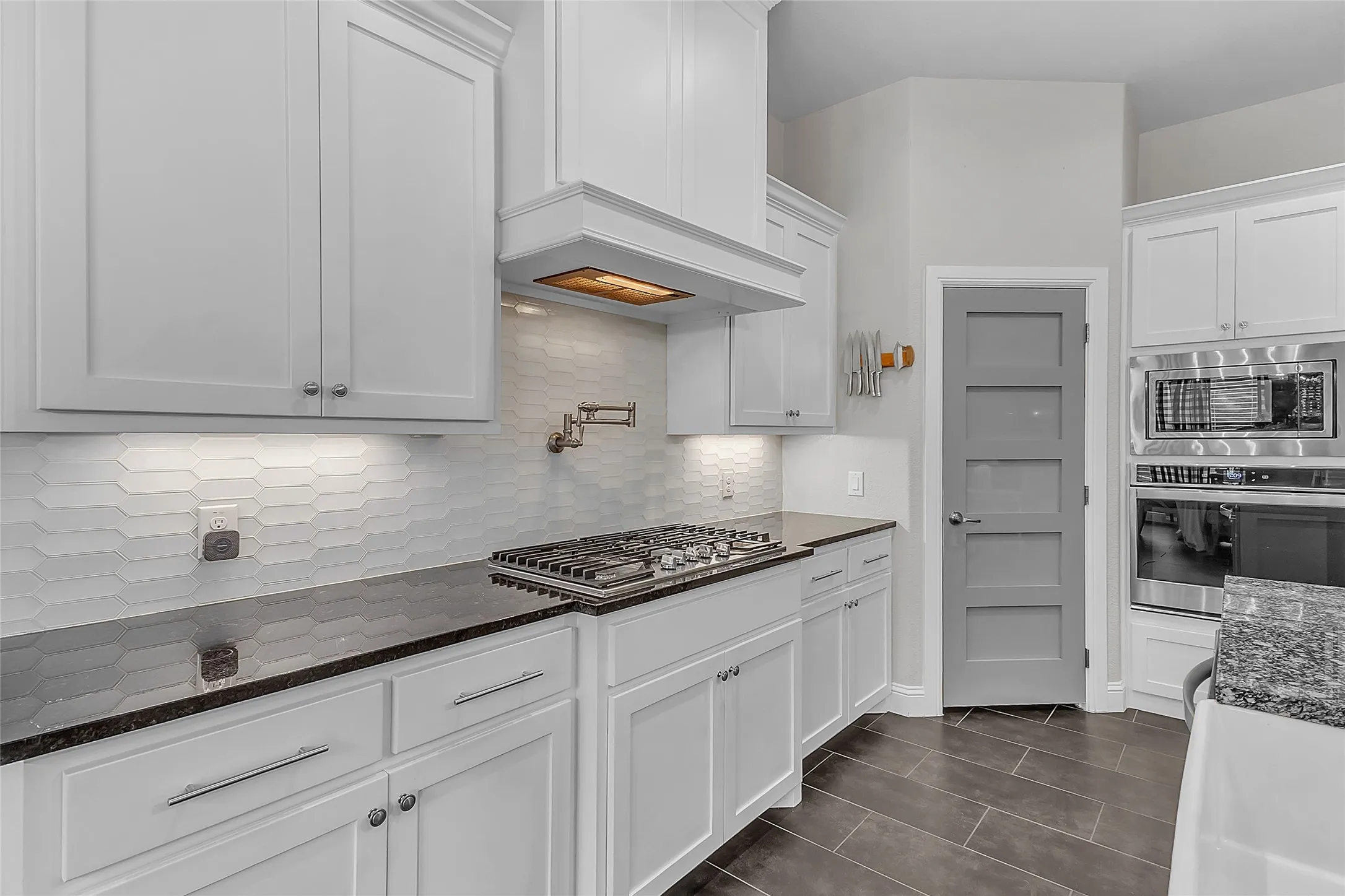 Kitchen featuring shaker cabinetry, gas range, generous-sized walk-in pantry with paneled door, granite countertops, a gas range with a pot filler faucet, stainless steel built-in appliances, and a gray paneled door