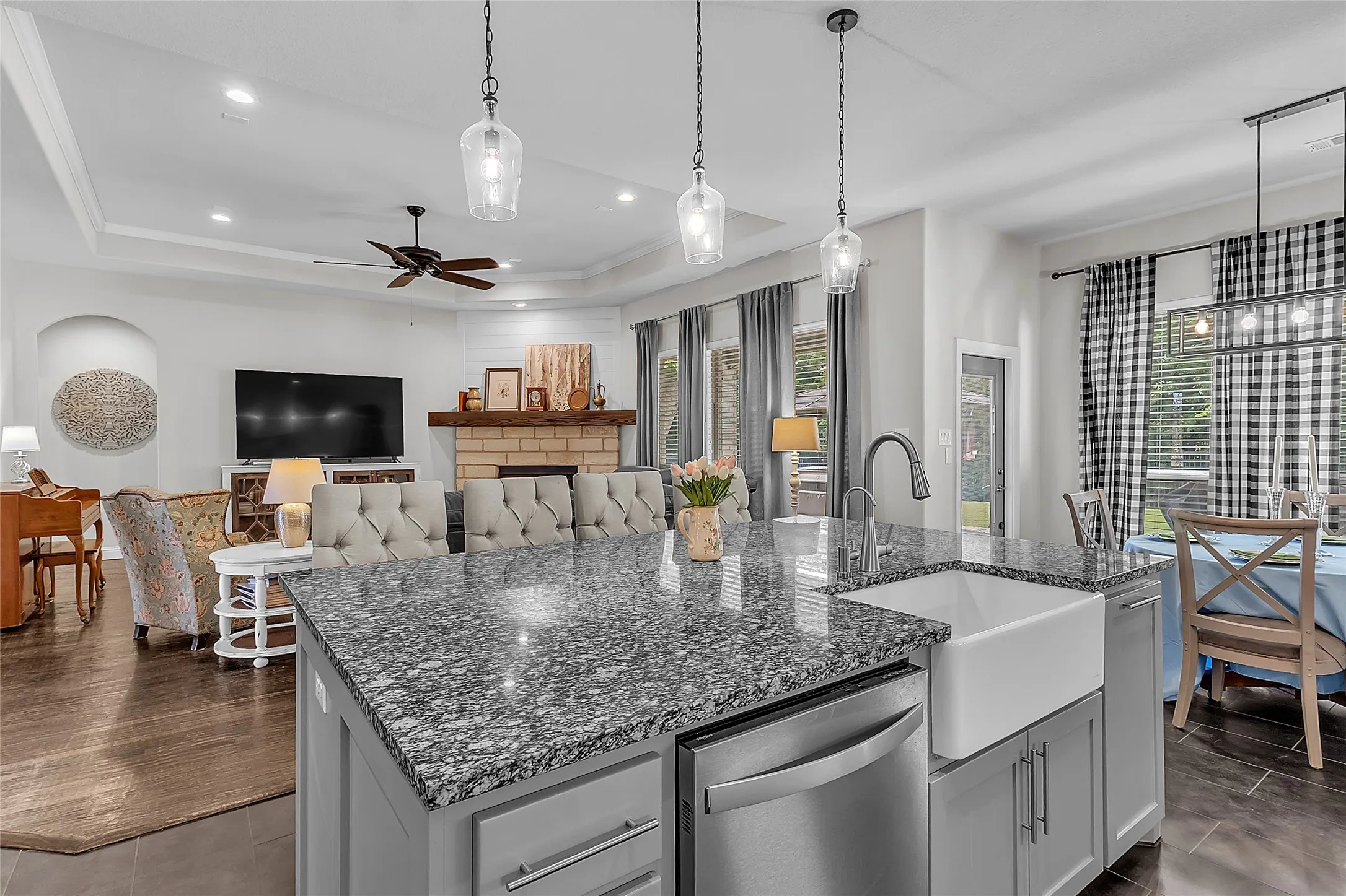 Kitchen featuring a large island with a granite countertop, shaker-style cabinetry with ample storage, integrated stainless steel appliances, and dark tile flooring overlooking main living and dining areas and back door