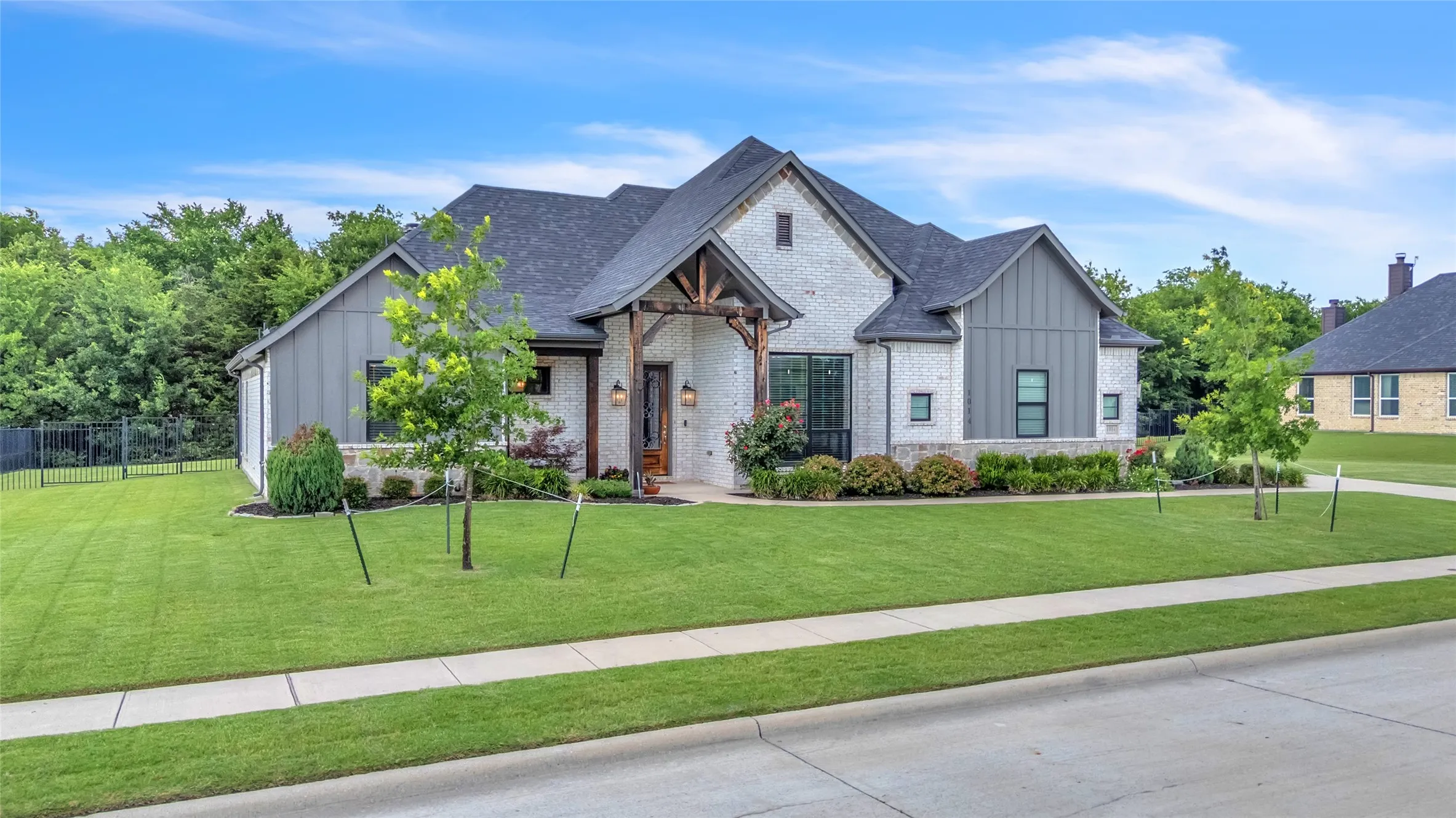 Modern farmhouse style exterior featuring brick, board & batten siding, and a stone exterior. Also shown is the covered front porch and elevated landscaping.