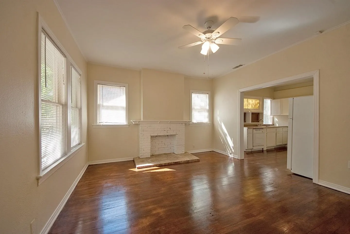 A spacious living room featuring hardwood floors, several windows, a fireplace and a ceiling fan, creating a bright and airy atmosphere.