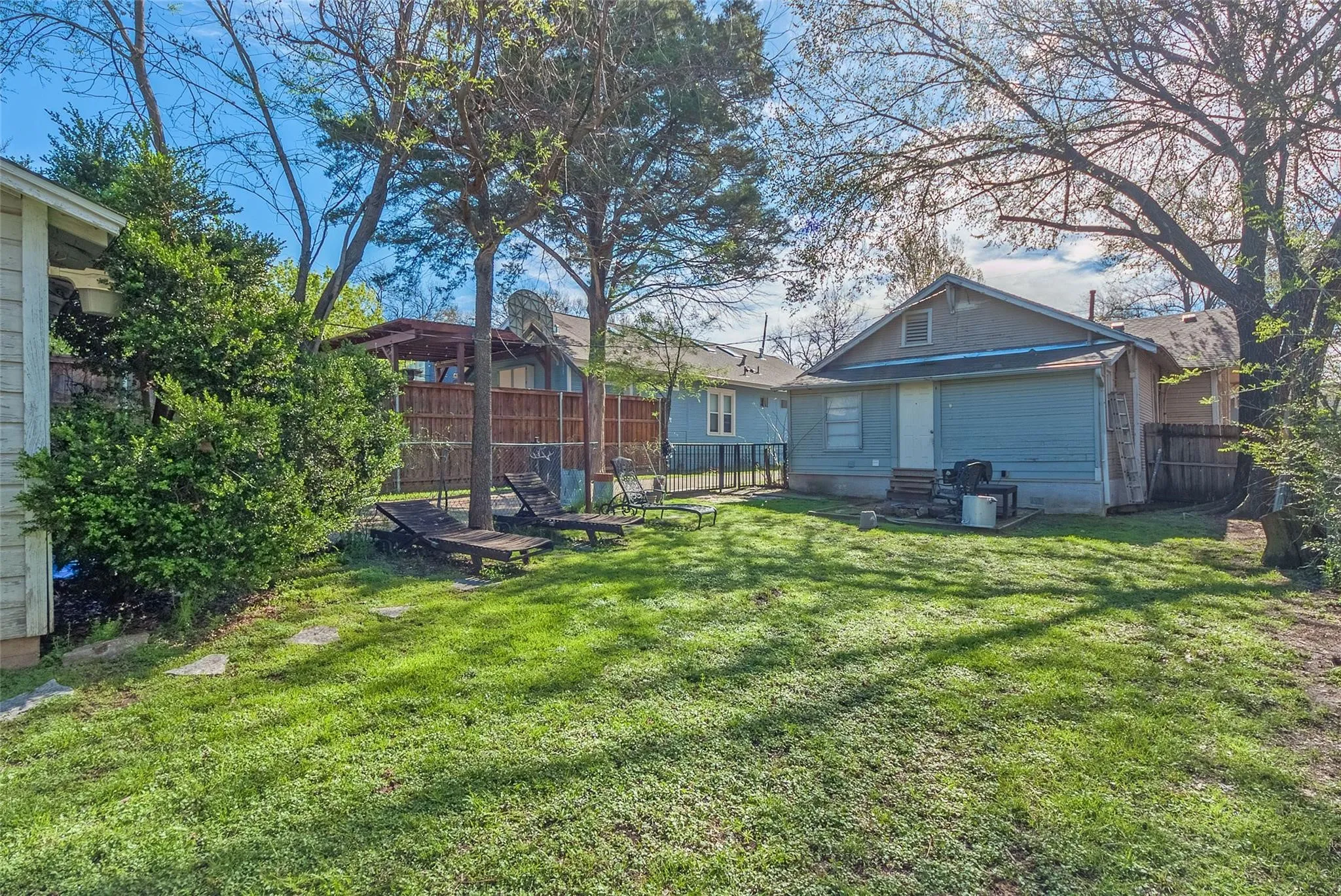 A spacious backyard with trees featuring a patio area and a grill, perfect for outdoor cooking and relaxation.