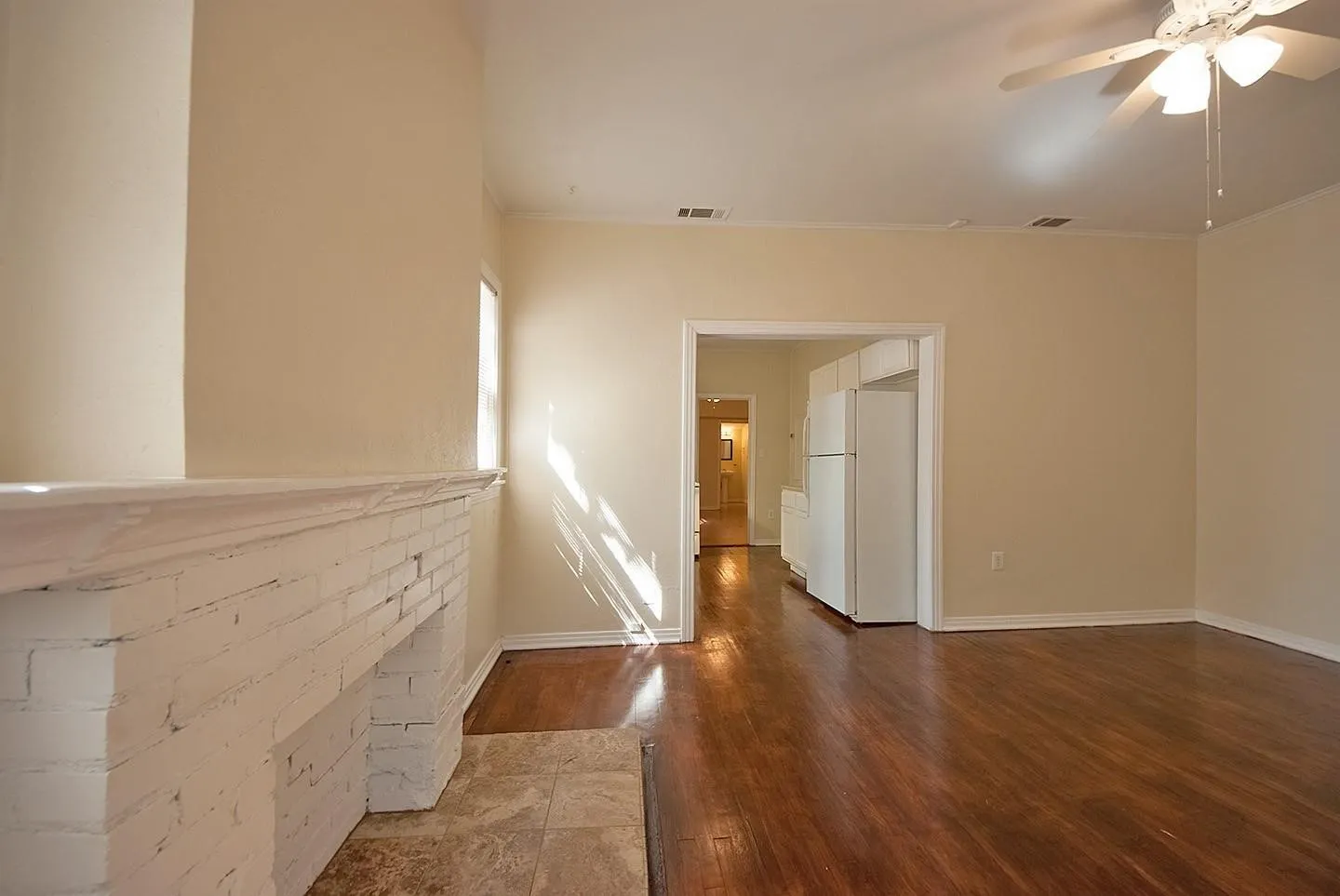 A spacious living room featuring hardwood floors, a fireplace and a ceiling fan, creating a bright and airy atmosphere.