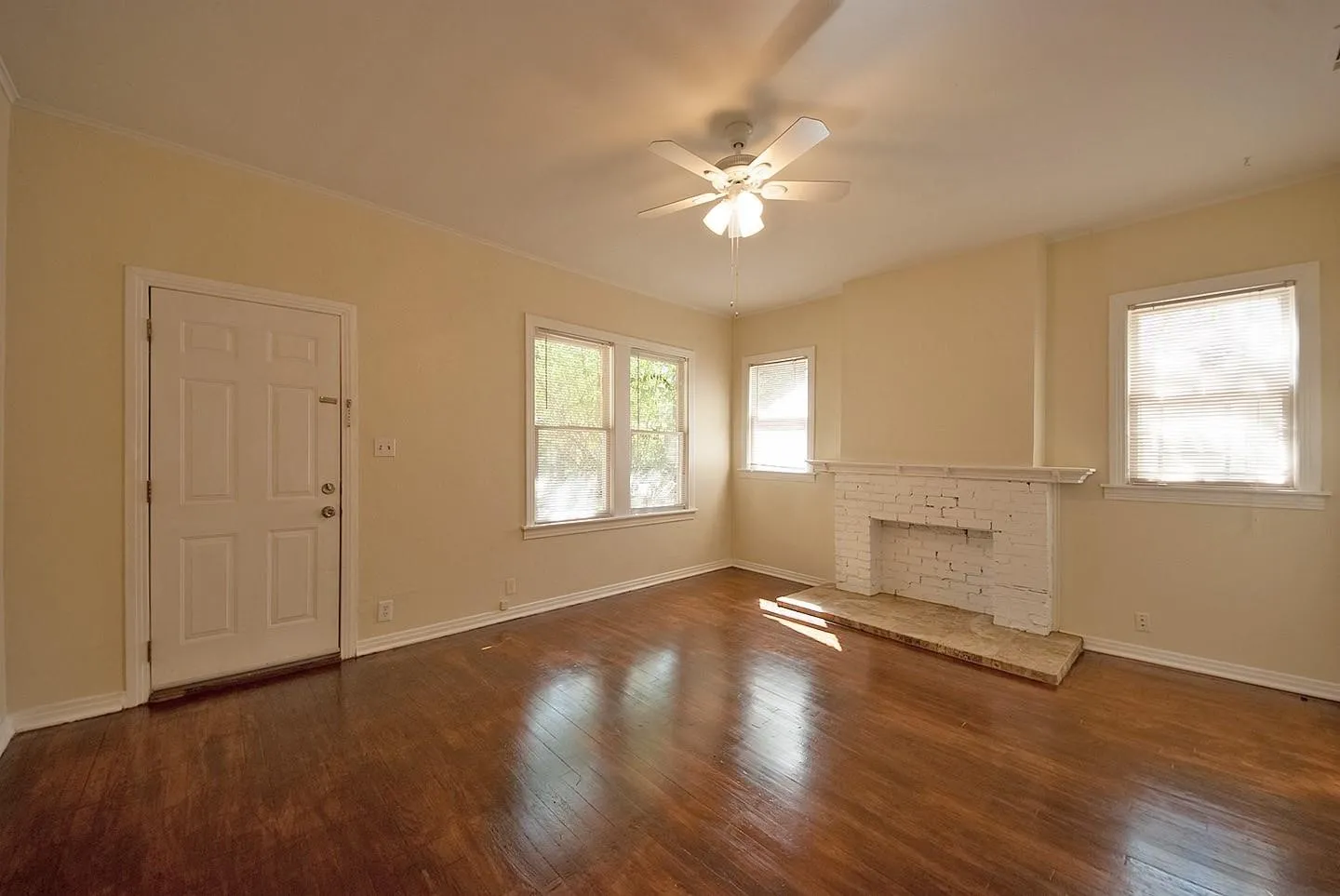 A spacious living room featuring hardwood floors, several windows, a fireplace and a ceiling fan, creating a bright and airy atmosphere.