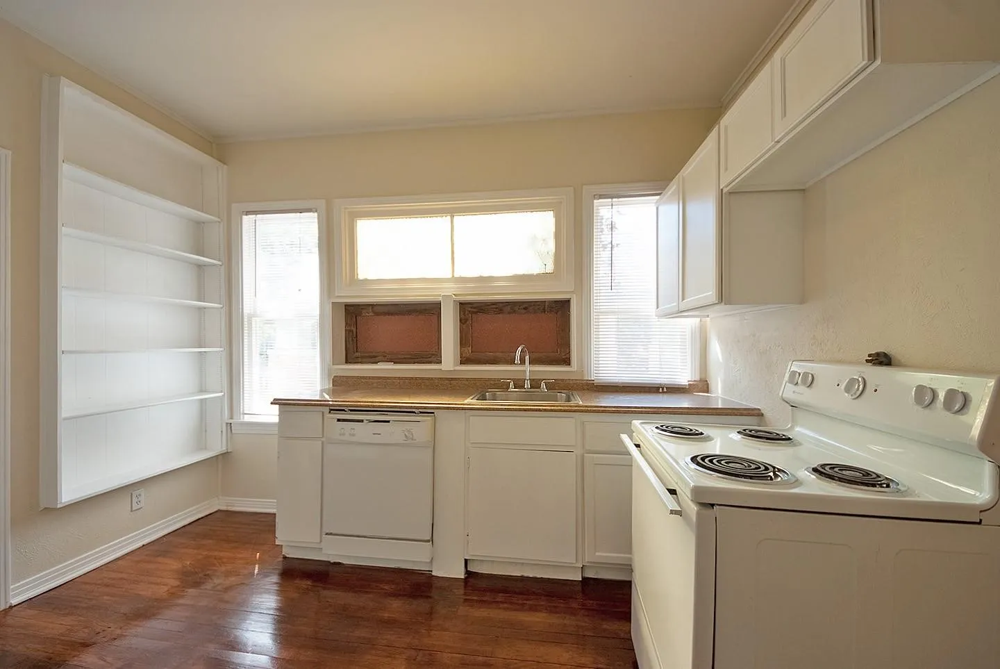 A cozy kitchen with white cabinets and shelves, dishwasher and a stove, creating a clean and inviting cooking space.