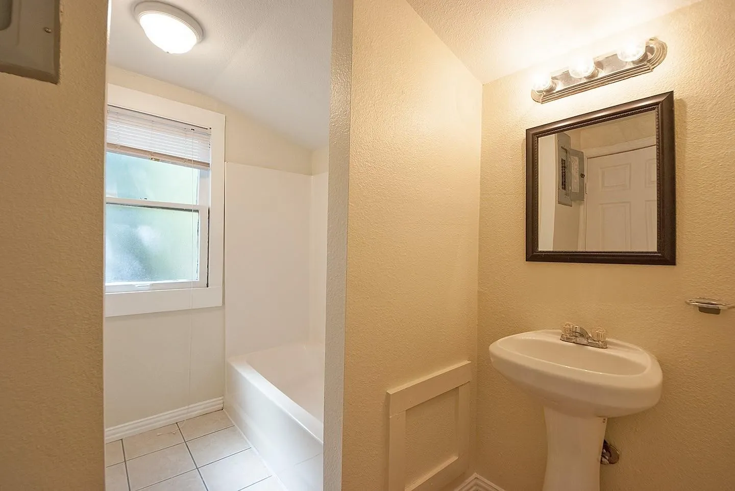 A bright bathroom with a sink, bathtub, and a window for ventilation and natural light.
