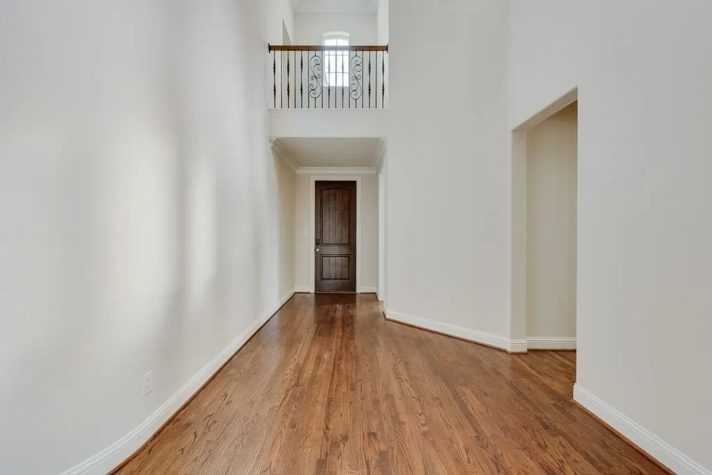 Two-story foyer featuring wood-finish flooring, white baseboards, crown molding, and a dark wood door