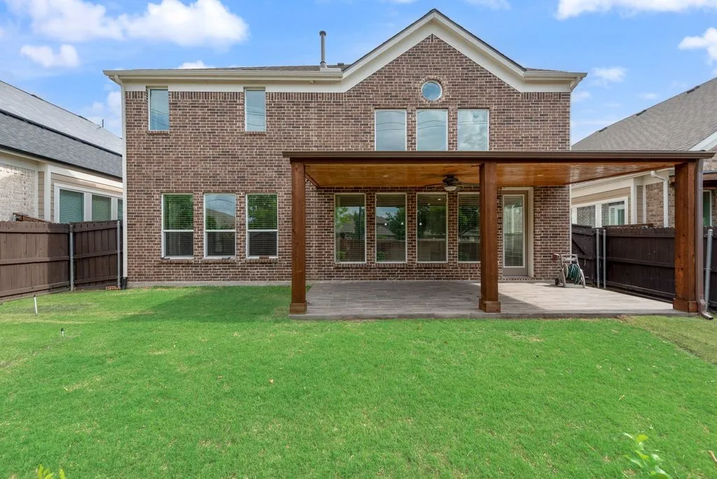 Expansive backyard featuring a manicured lawn, a large paver patio, and a covered pergola with a ceiling fan