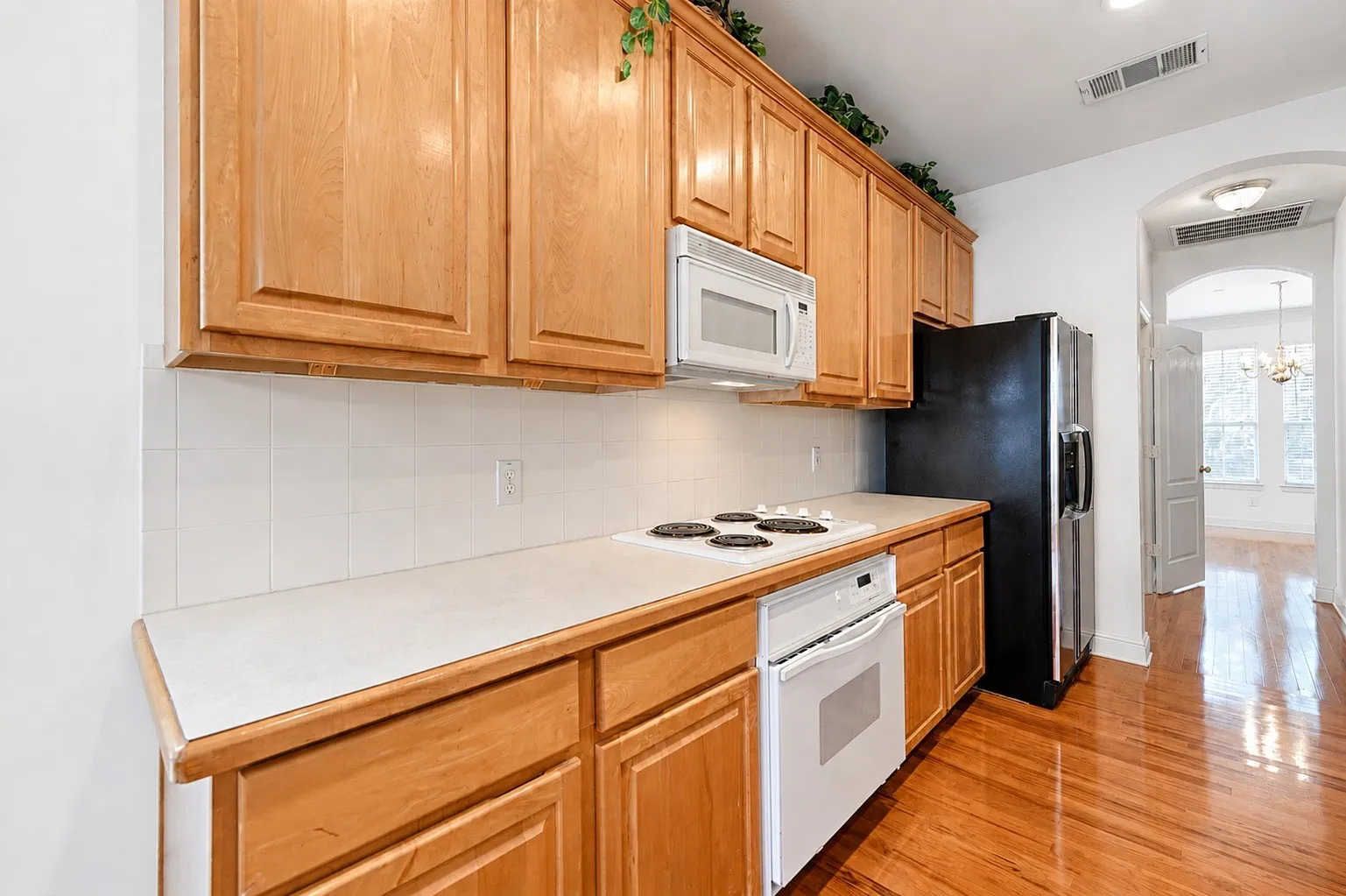 Kitchen featuring warm wood cabinetry, white tile backsplash, light-toned countertops, white electric range, and a stainless steel refrigerator