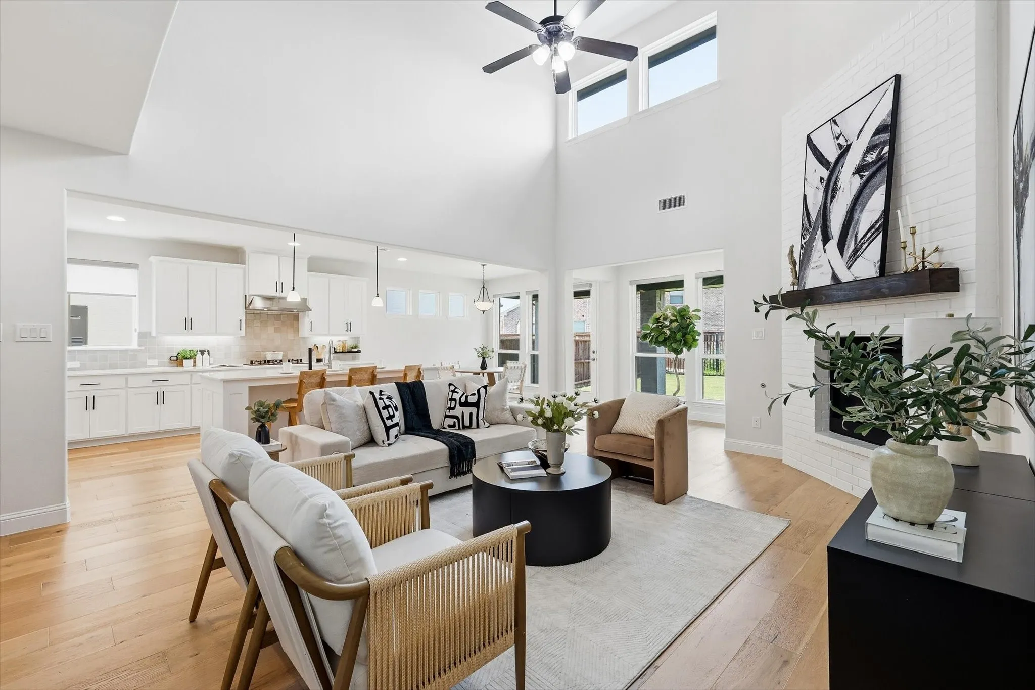 Two-story living area featuring a vaulted ceiling with ceiling fan, a white brick fireplace with a dark wood mantel, and wood-finish flooring