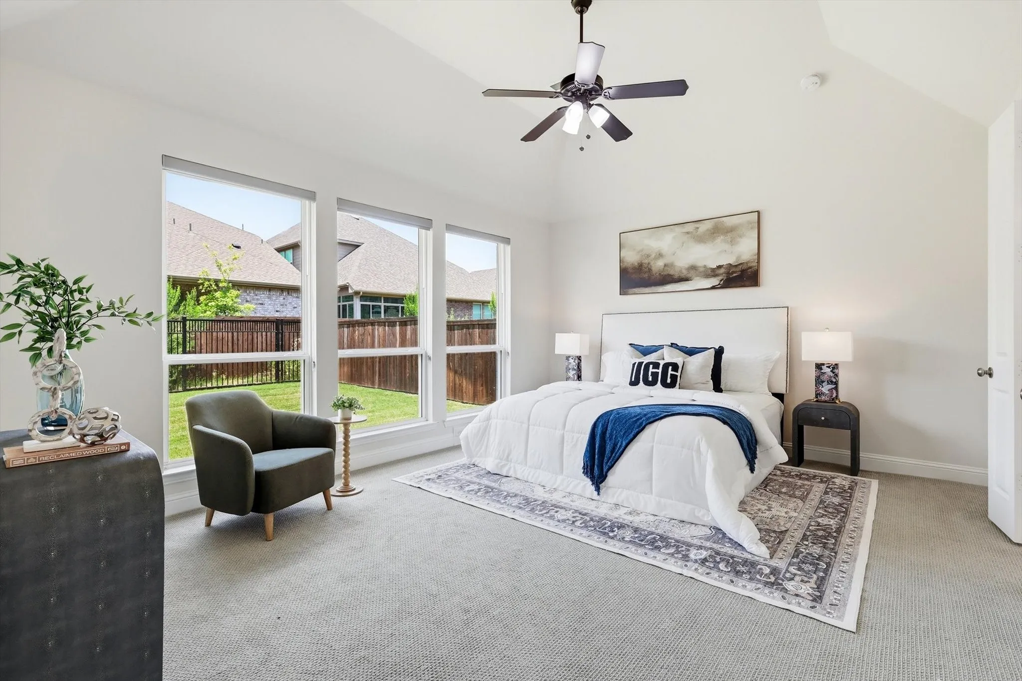 Vaulted ceiling bedroom featuring expansive windows, neutral tone carpeting, a ceiling fan with light fixture, and a white paneled door