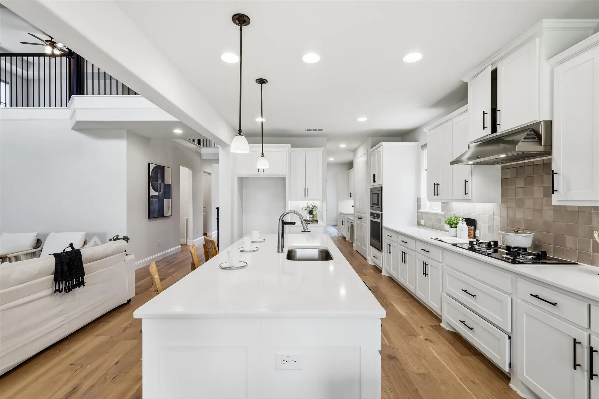Modern kitchen featuring a large central island, white cabinetry with matte black hardware, stainless steel appliances, and wood-finish flooring