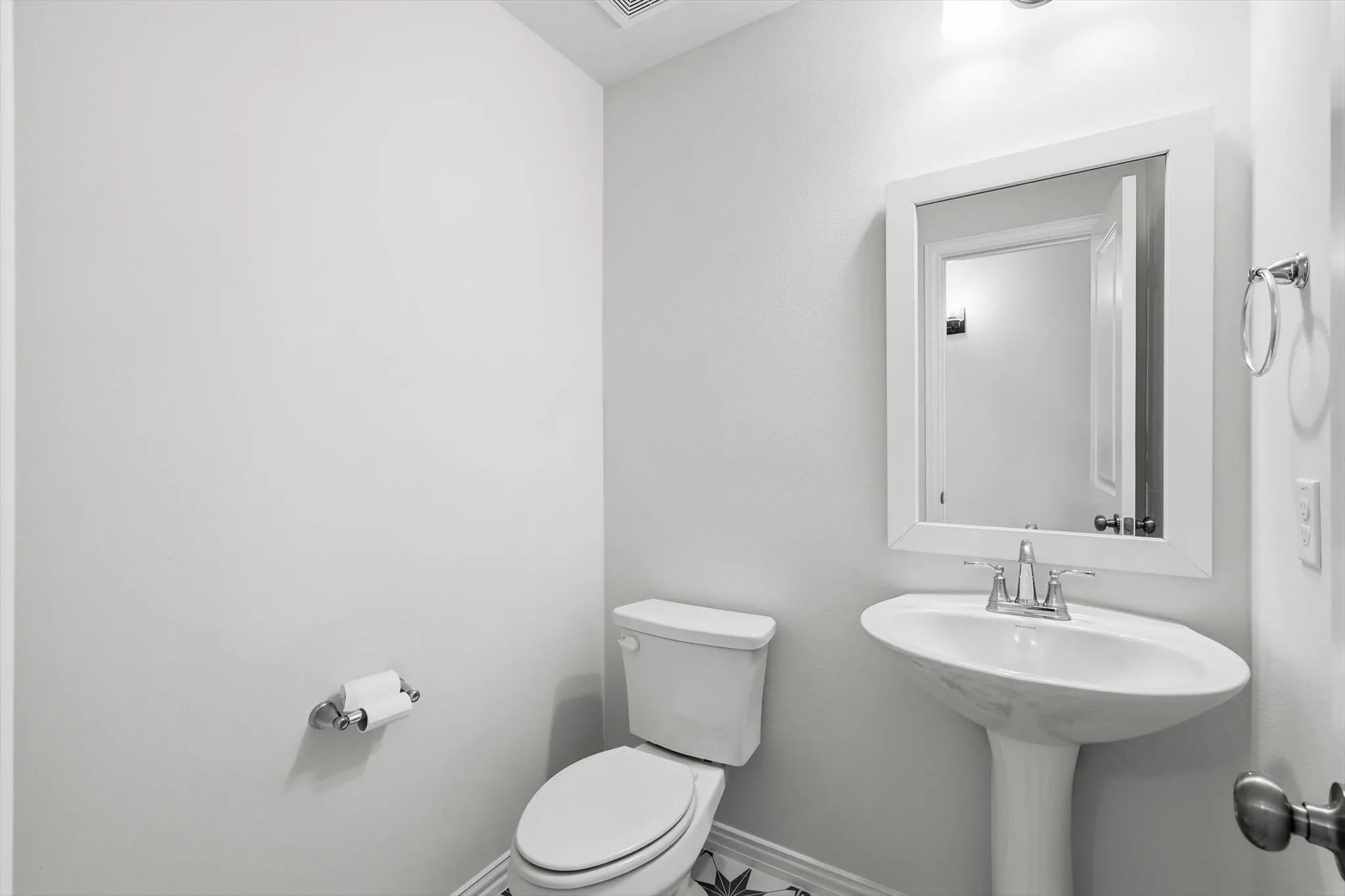 Pedestal sink with chrome faucet, framed vanity mirror, and white toilet