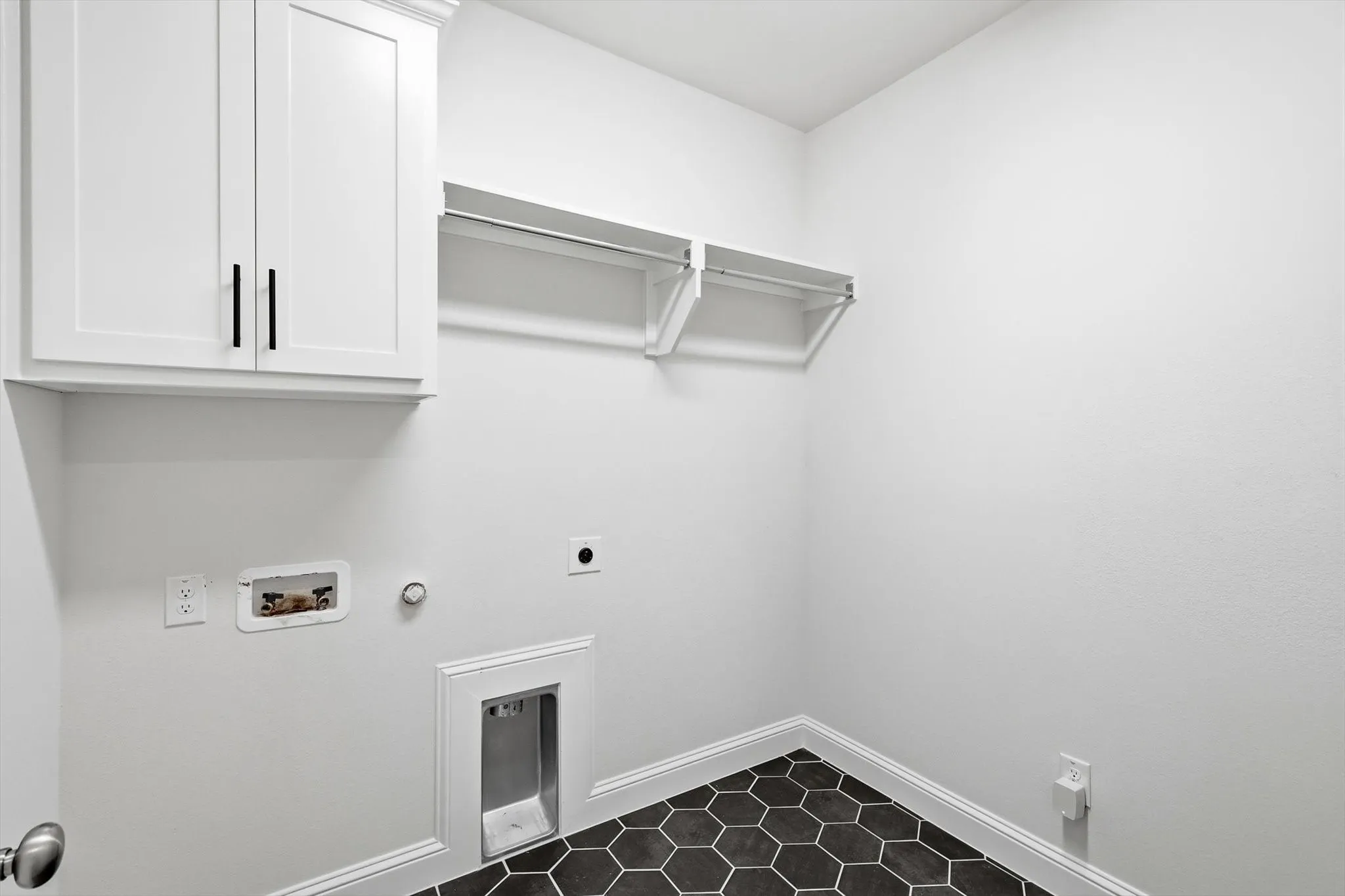 Dedicated laundry space featuring white cabinetry with dark hardware, a clothes hanging rod, hexagonal floor tiles, and a dryer vent