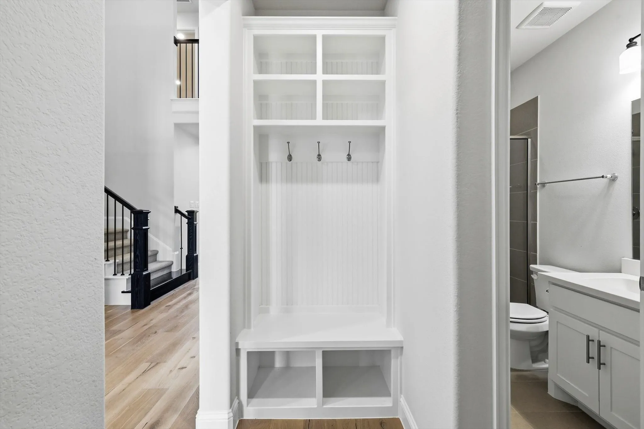 Built-in white storage unit featuring shelving, hooks, and bench seating with cubbies