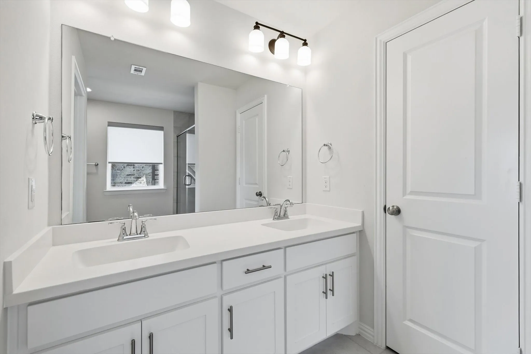 Double vanity with integrated sinks, white cabinetry, chrome fixtures, and a large wall-mounted mirror